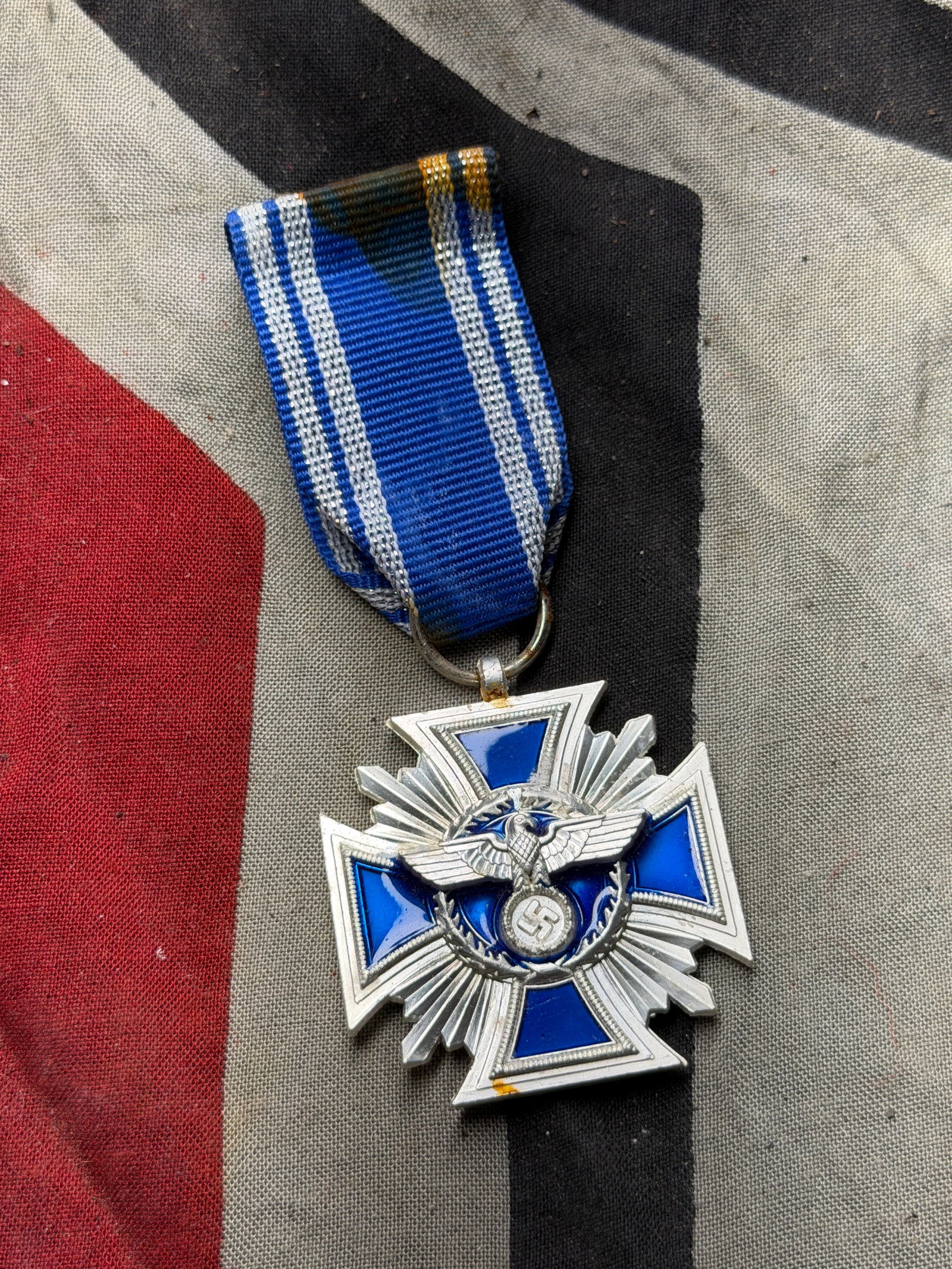 WW2 German Faithful Service Decoration — Civil Merit Cross (Blue-Enamel Version): This is a silvered metal and blue-enamel cross suspended from a blue and white striped ribbon. The obverse displays a stylized German national emblem, while the reverse bears the inscription “Treue 