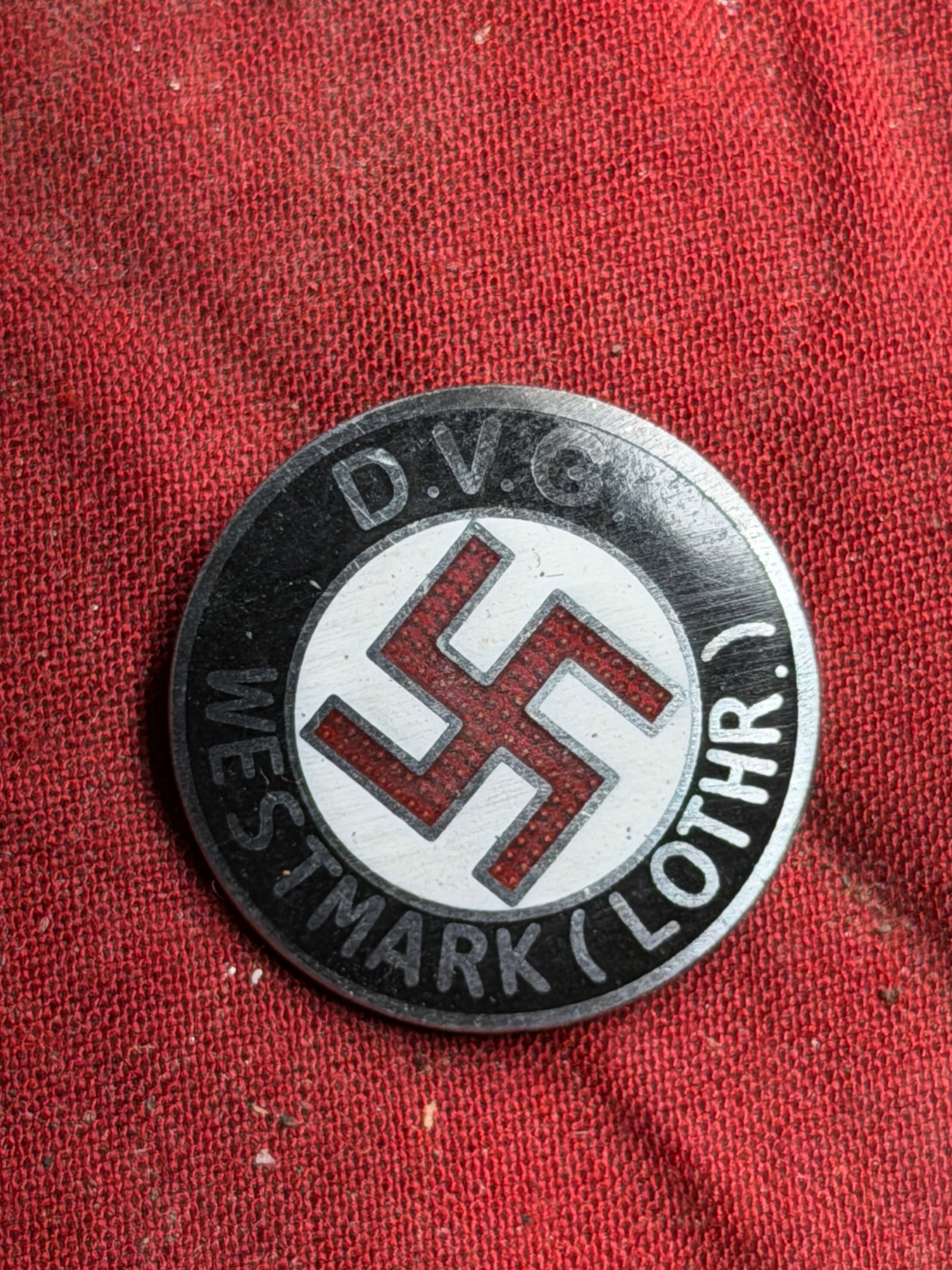 WW2 German Regional Membership Badge — D.V.G. Westmark (Lothringen) By W. Redo Saarlautern: This is a circular metal membership badge associated with a regional organization in Westmark (Lorraine), manufactured by W. Redo, Saarlautern as stamped on the reverse. The badge features enamel deta