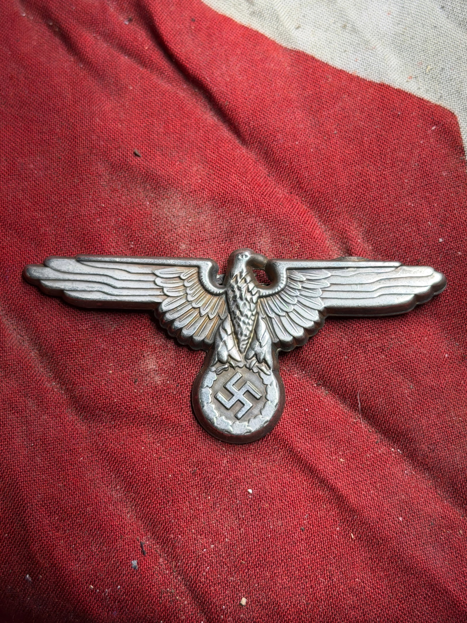 Waffen-SS Visor Cap Eagle Badge, WW2 Germany, Circa 1939–1945: This metal insignia depicts a stylized eagle with outstretched wings clutching a circular wreath. It served as the cap badge for the Waffen-SS visor cap, a key element of uniform design in Nazi German