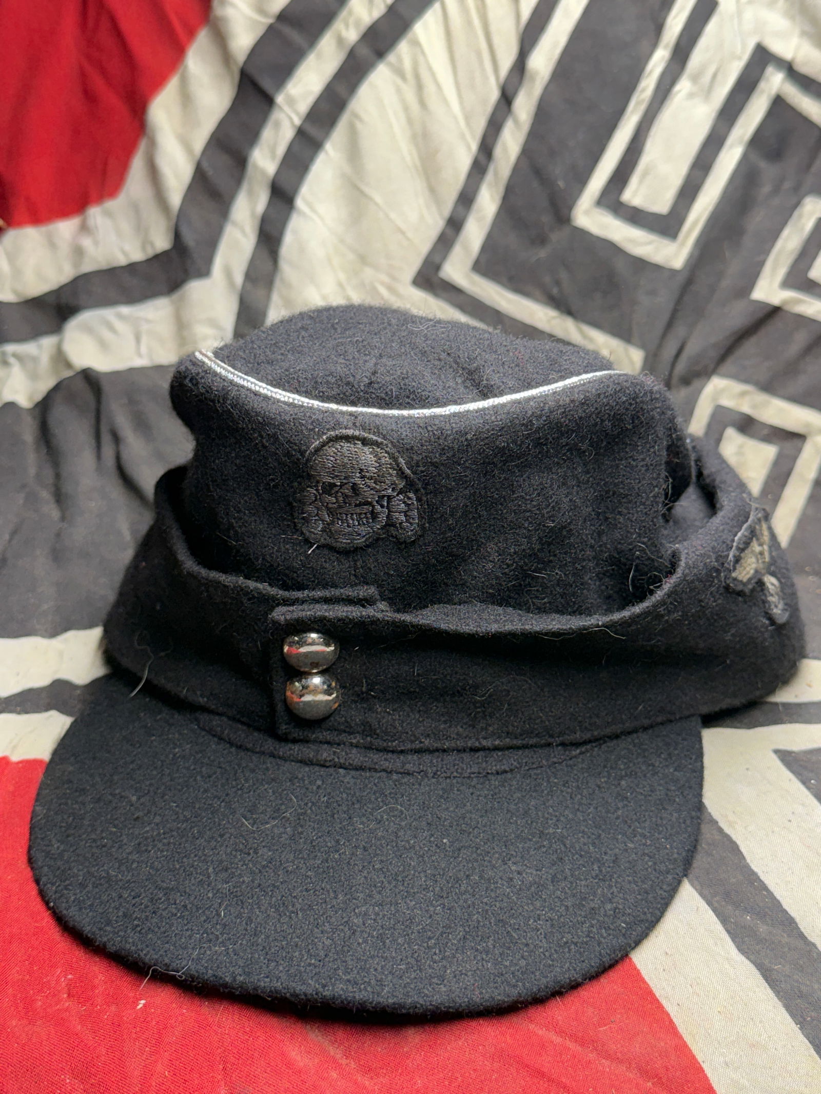 WWII German Panzer Officer’s Field Cap – Black Wool, RZM Marked Interior: This is a World War II-era German Panzer officer’s field cap (Feldmütze) constructed of black wool, complete with silver piping, embroidered skull insignia, and national eagle emblem on the front.