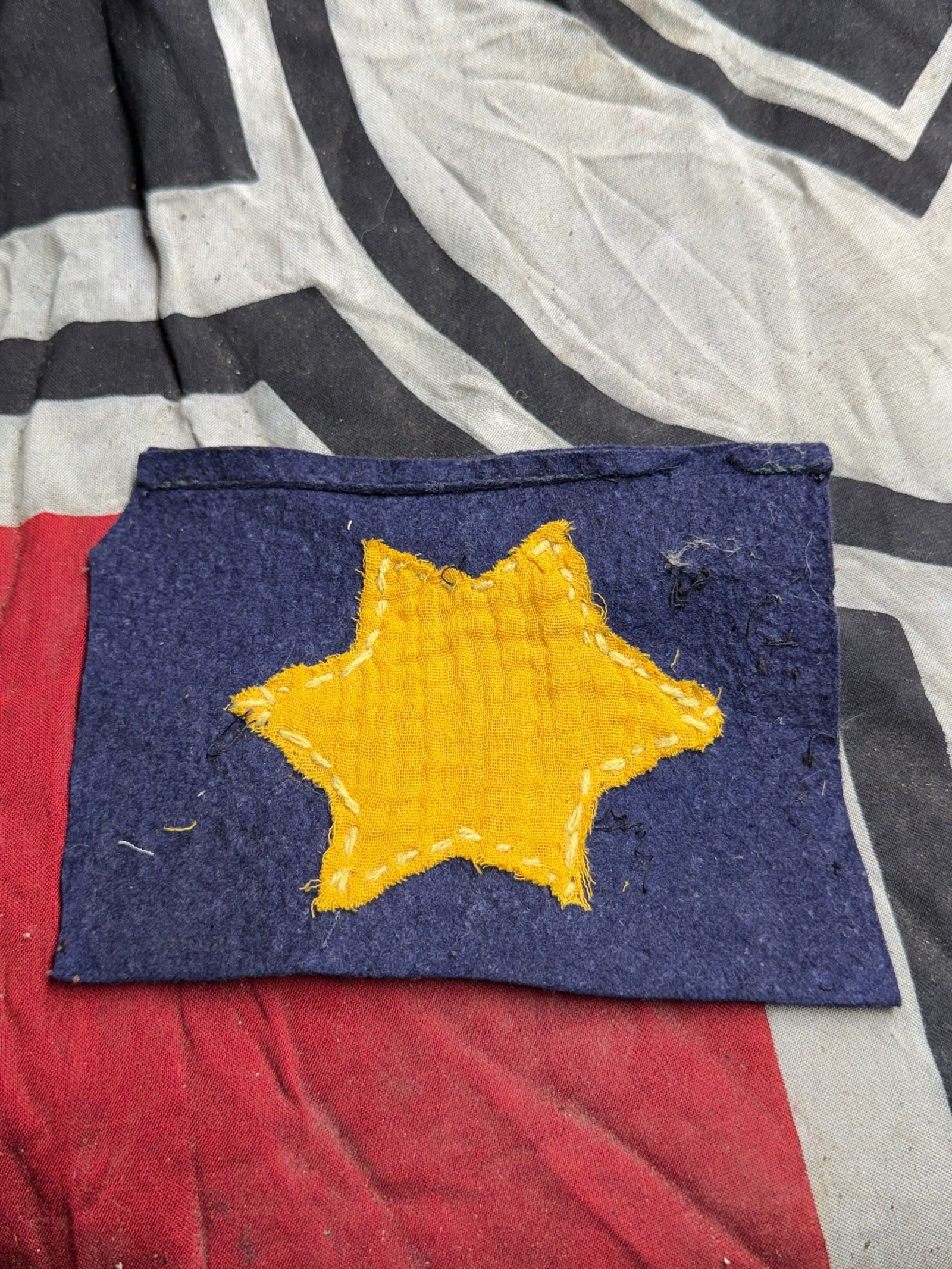 Rare WW2 German Yellow Star Patch, Holocaust Era (c. 1940s): This textile piece consists of a yellow six-pointed star sewn by hand onto a dark blue fabric backing. The star is crudely stitched with light thread, and the patch shows visible wear and fraying cons
