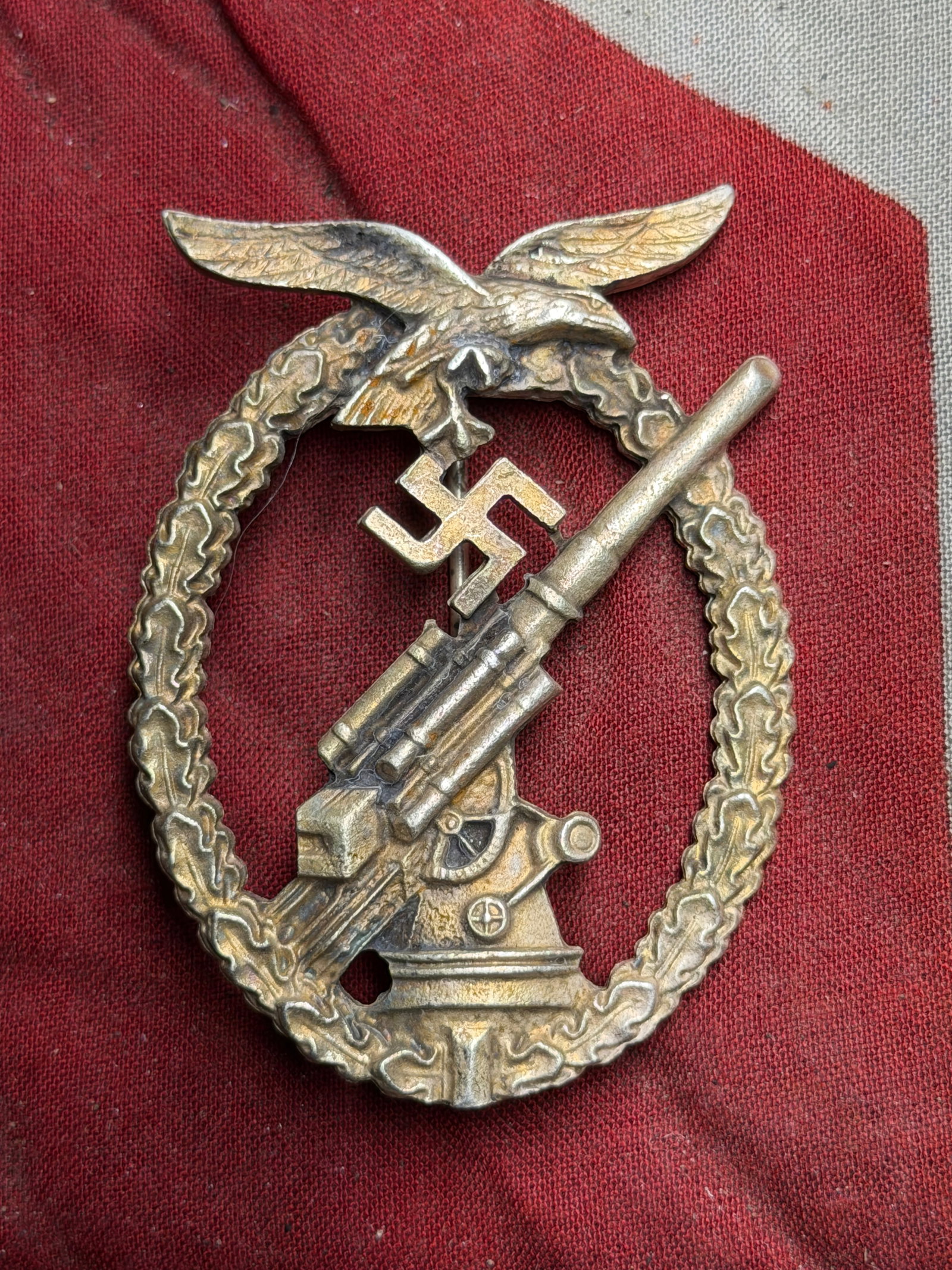 German Anti-Aircraft Badge (Flak Badge), World War II Period: This metallic badge depicts an anti-aircraft gun within a wreath of oak leaves, surmounted by an eagle. It was originally associated with Luftwaffe anti-aircraft personnel during the Second World War 