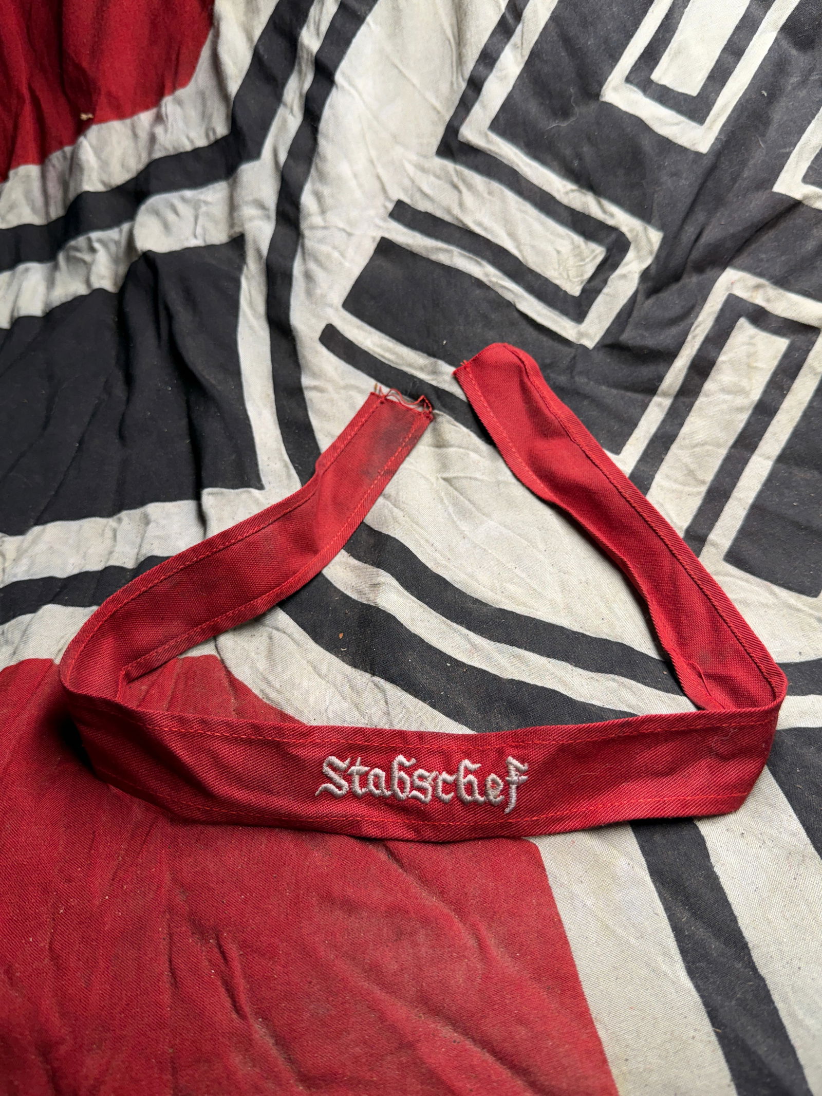 WW2 German Paramilitary Armband with “Stabschef?? Inscription, 1930s–1940s: This red armband features the embroidered title “Stabschef” (“Chief of Staff”) in white Gothic-style lettering. The band is made of cotton fabric with folded and stitched edges, showin
