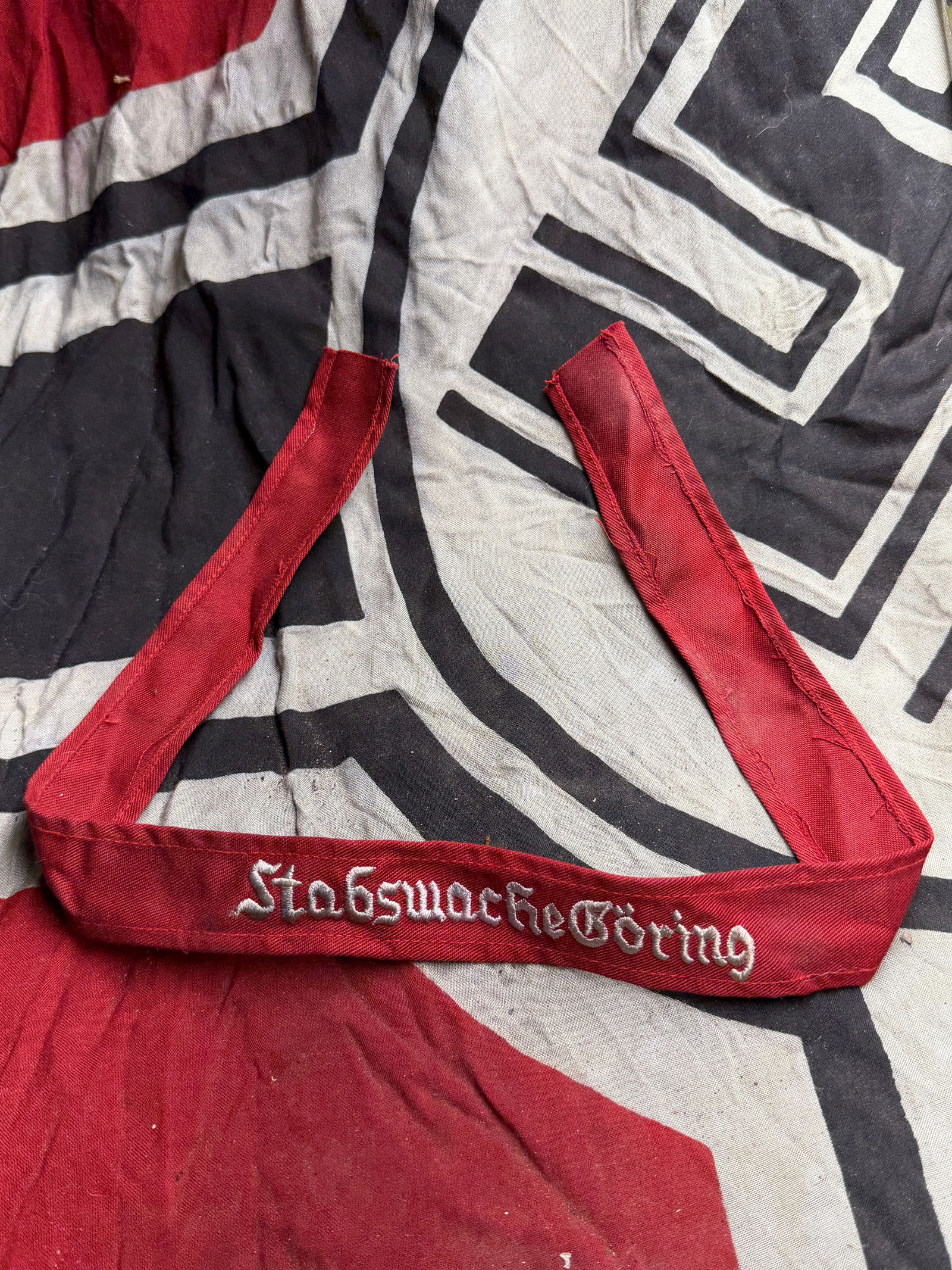 WW2 German Stabswache Goring Cuff Title: WW2 German Stabswache Goring Cuff Title. This red fabric cuff title features the embroidered text “Stabswache Göring” in silver-grey thread, stitched in Gothic-style script. The band is made