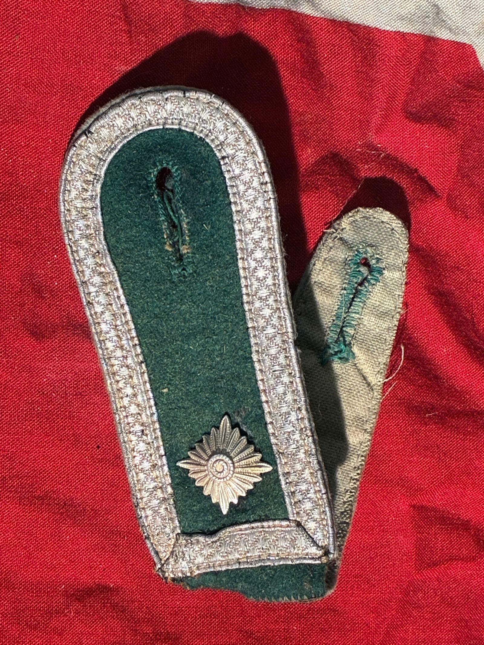 WW2 German Police Officer Shoulder Board (c. 1936–1945): This shoulder board belonged to a uniform of the Ordnungspolizei (Order Police) in Nazi Germany. Constructed with a dark green wool base and edged with silver/aluminum wire braid, the board features a