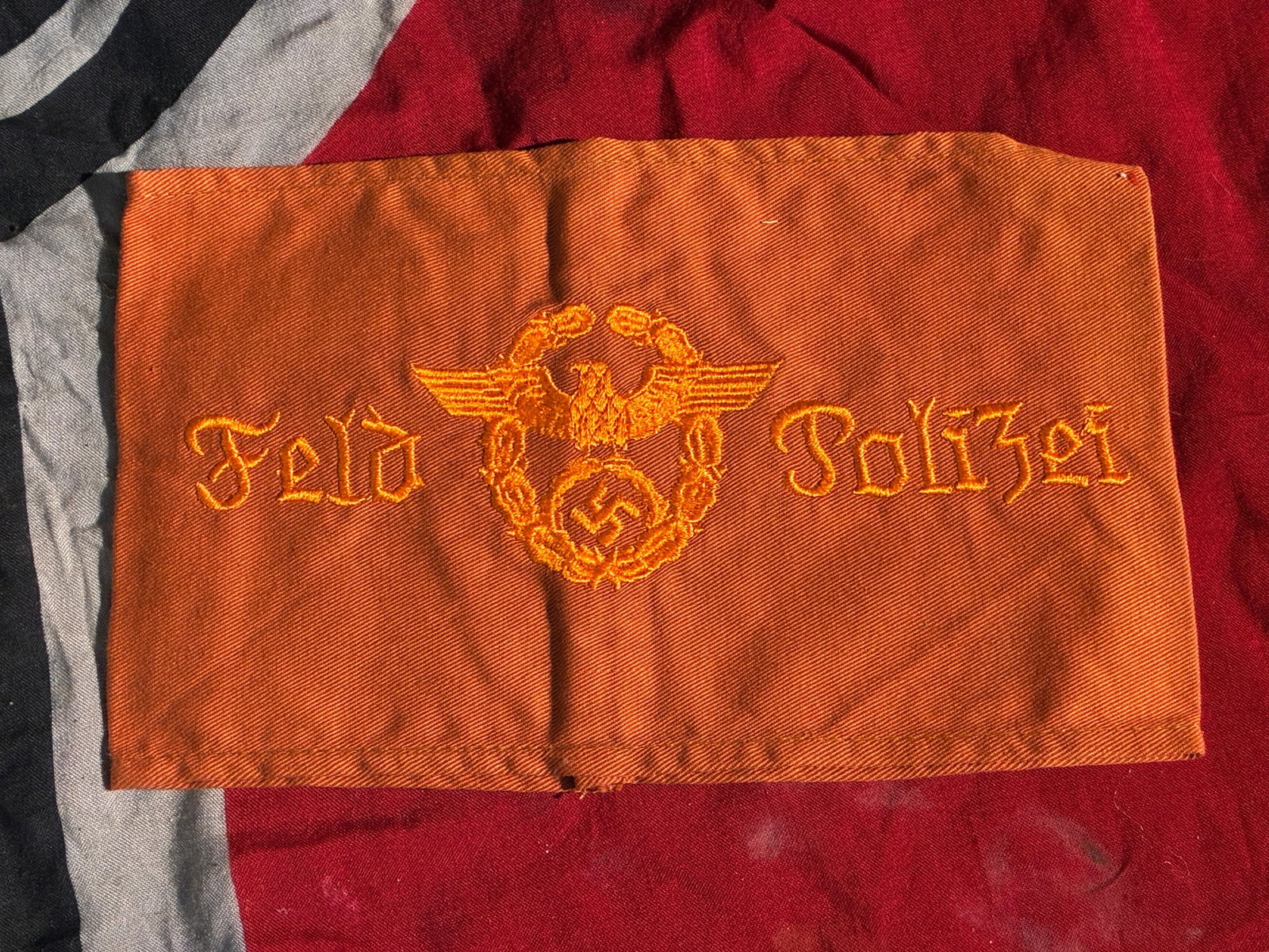 WW2 German Field Police Identification Armband (Feldpolizei), c. 1940–1945: This orange cloth armband, embroidered in golden-yellow thread with the inscription “Feld Polizei” and the German national eagle and wreath emblem, served as an identifying insignia for member