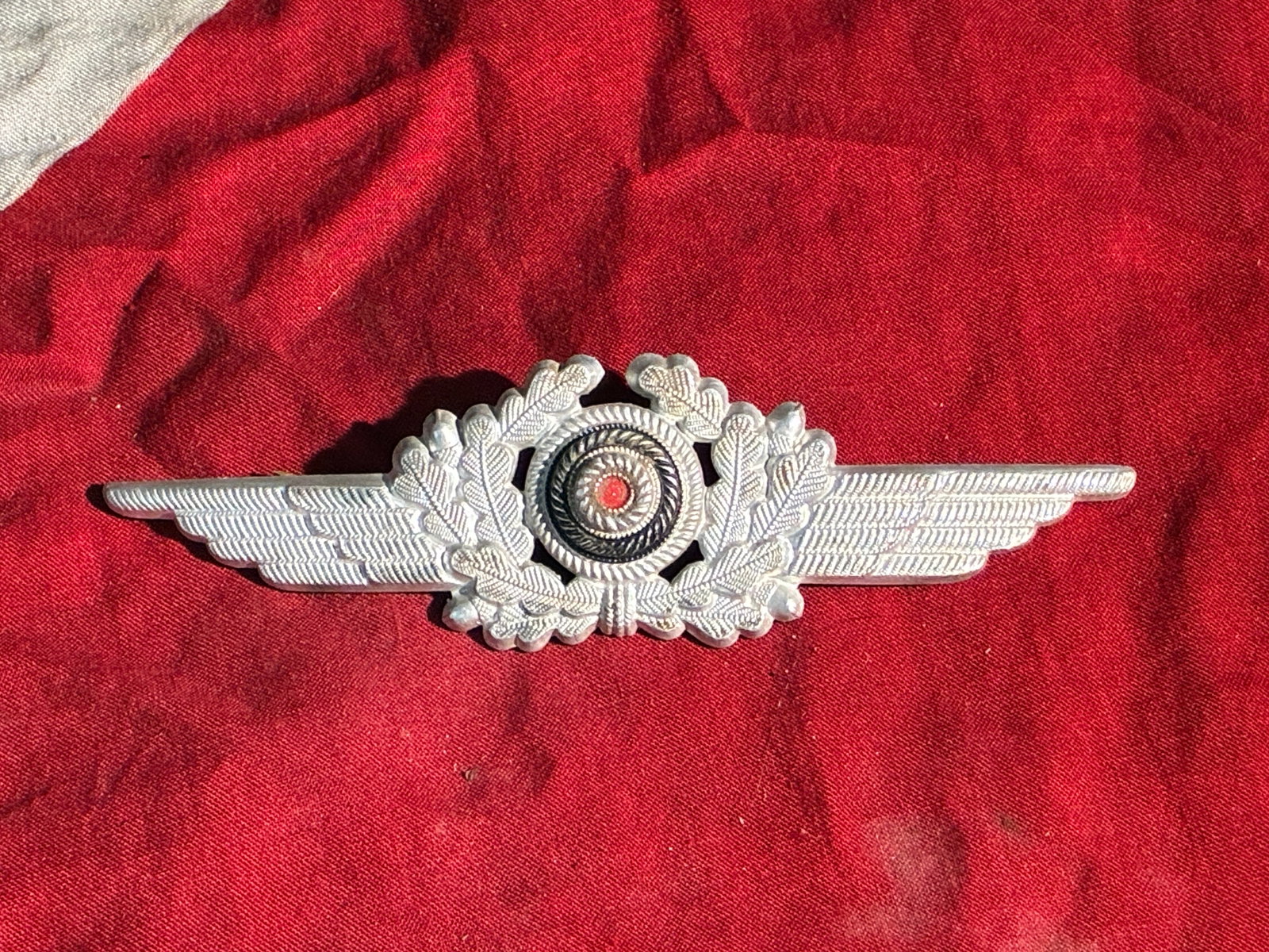 WW2 German Luftwaffe Officer’s Visor Cap Cockade & Wreath (c. 1935–1945): This aluminum cap insignia, featuring an oak-leaf wreath flanked by stylized wings and centered with the national red-white-black cockade, was worn on the service visor caps of Luftwaffe officers duri