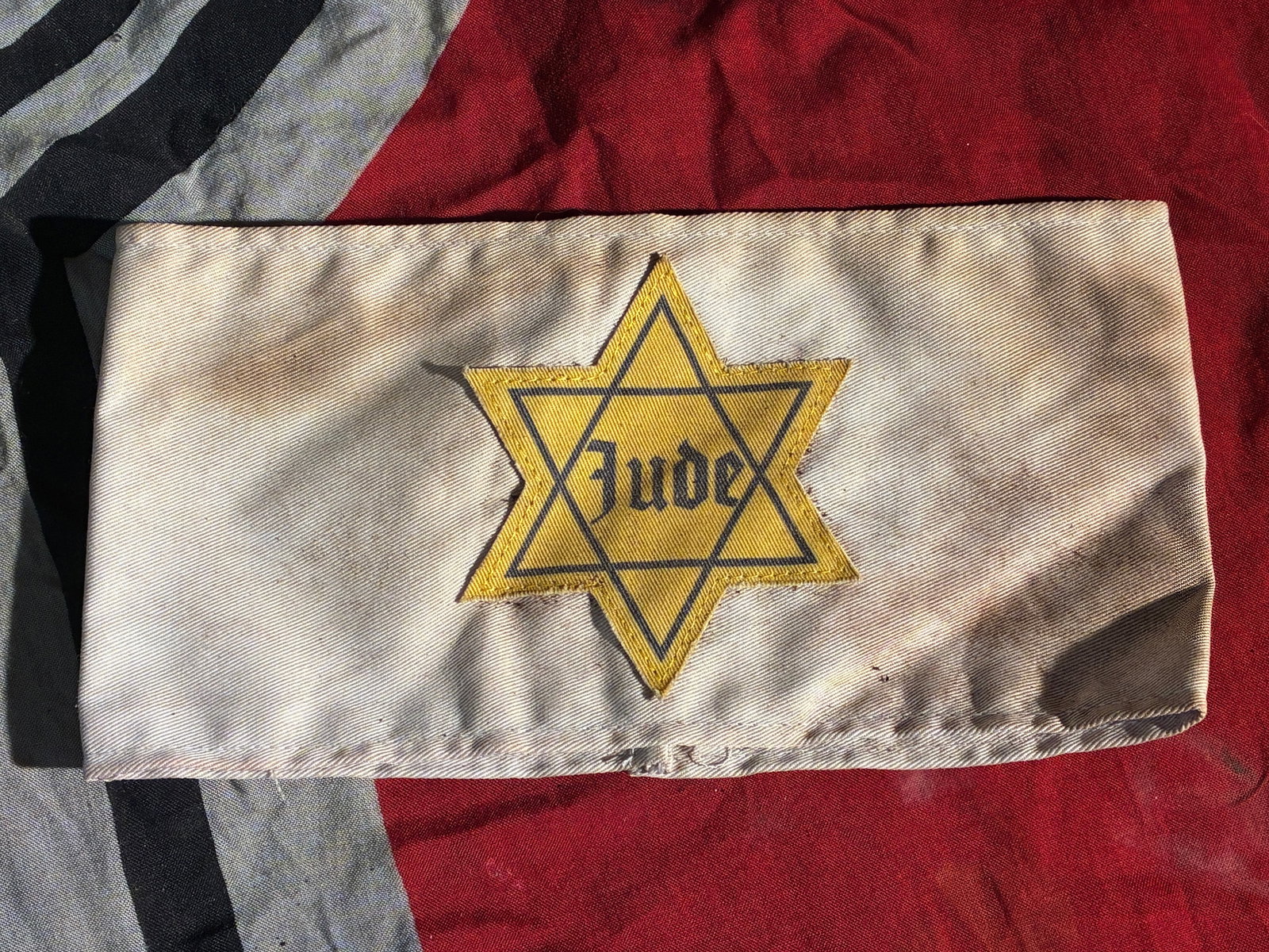 WW2 German Jewish Identification Armband (“Jude?? Armband), Nazi-Occupied Europe, c. 1941–1945: This cloth armband, bearing the yellow Star of David and the word “Jude” (“Jew” in German), is a stark and chilling artifact from the Holocaust and the broader system of persecution en