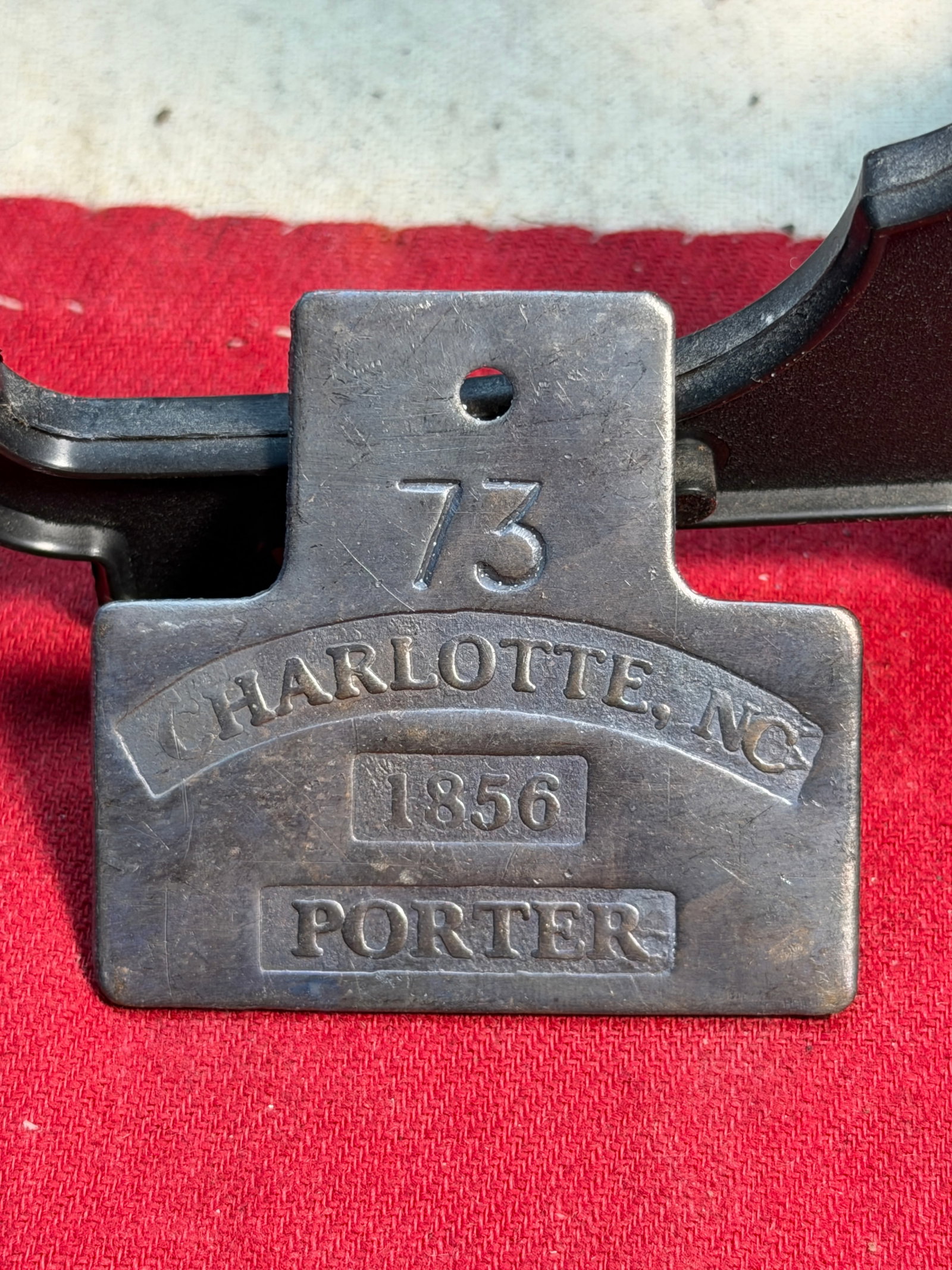 1856 Charlotte, North Carolina Slave Tag – Porter Servant Identification Badge No. 73: This rare 1856 servant identification tag, stamped “73 – CHARLOTTE, N.C. – PORTER”, is an original brass license badge once worn by an enslaved laborer in antebellum Charlotte. Such tags f