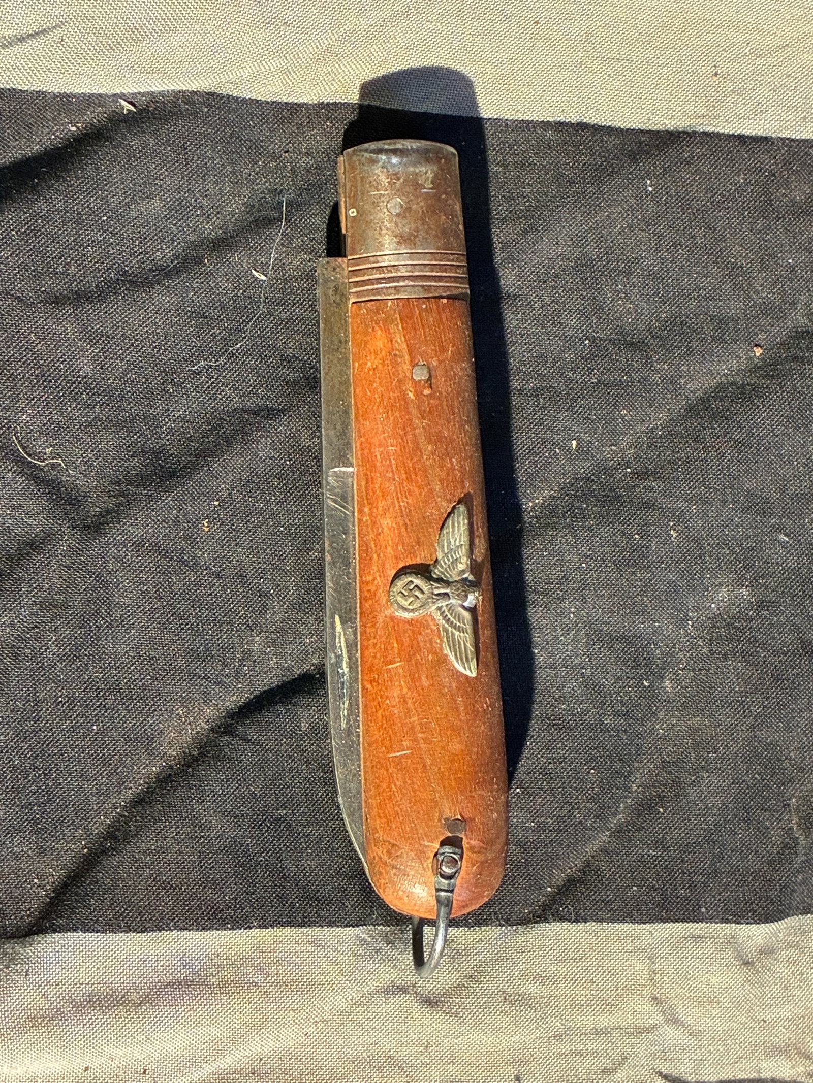 WW2 German Military Folding Knife with National Emblem (c. 1930s–1940s): This folding utility knife features a wooden handle fitted with a metal inlay depicting the German national eagle positioned above a swastika—an emblem used during the period of Nazi rule (1933–19