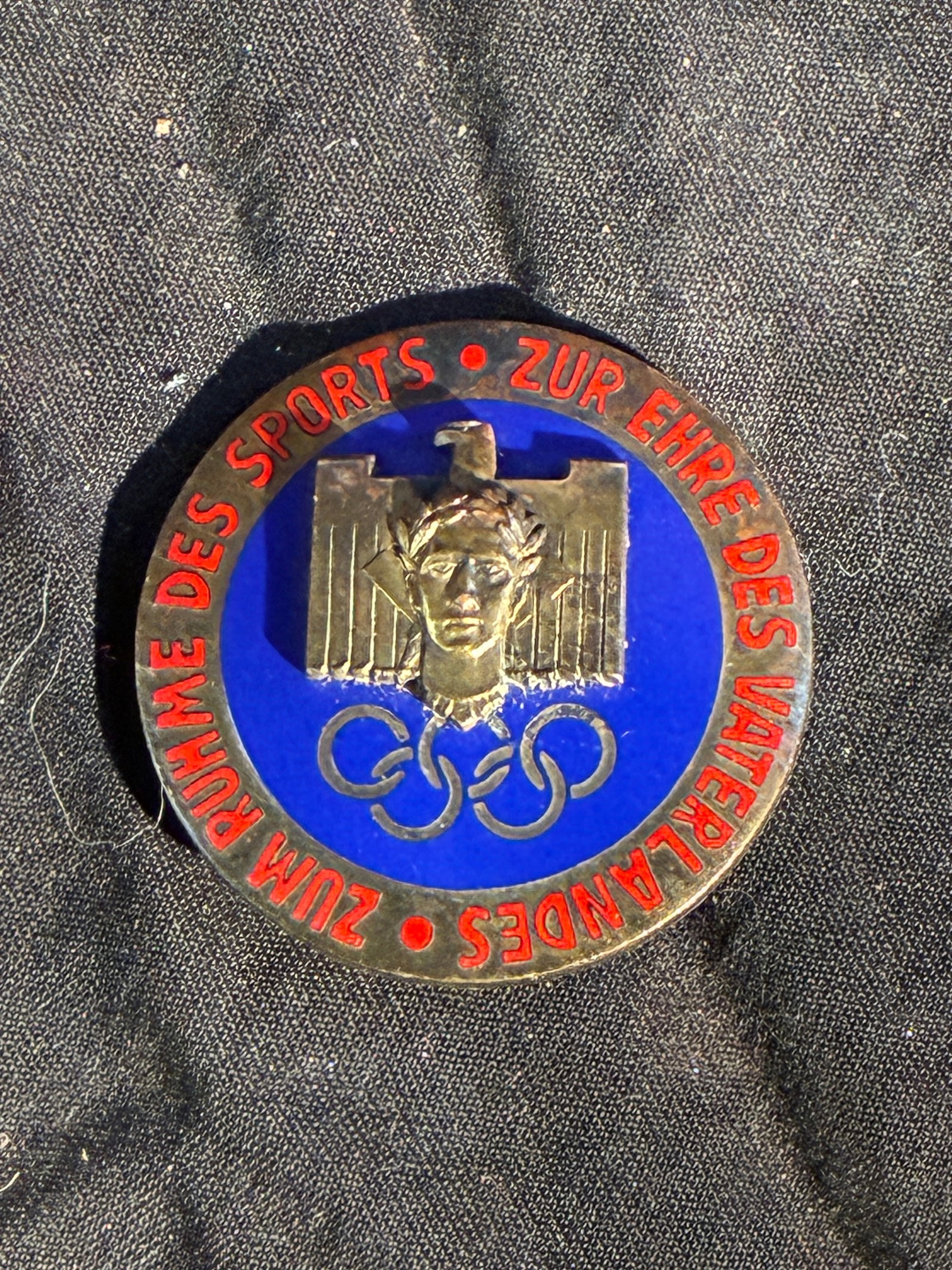 WW2 German 1936 Berlin Sports Merit Badge By W.A.R. & Co., München: This circular enamel badge was produced in Nazi Germany in conjunction with athletic and propaganda events surrounding the 1936 Berlin Olympic Games. The front features a stylized classical head crown