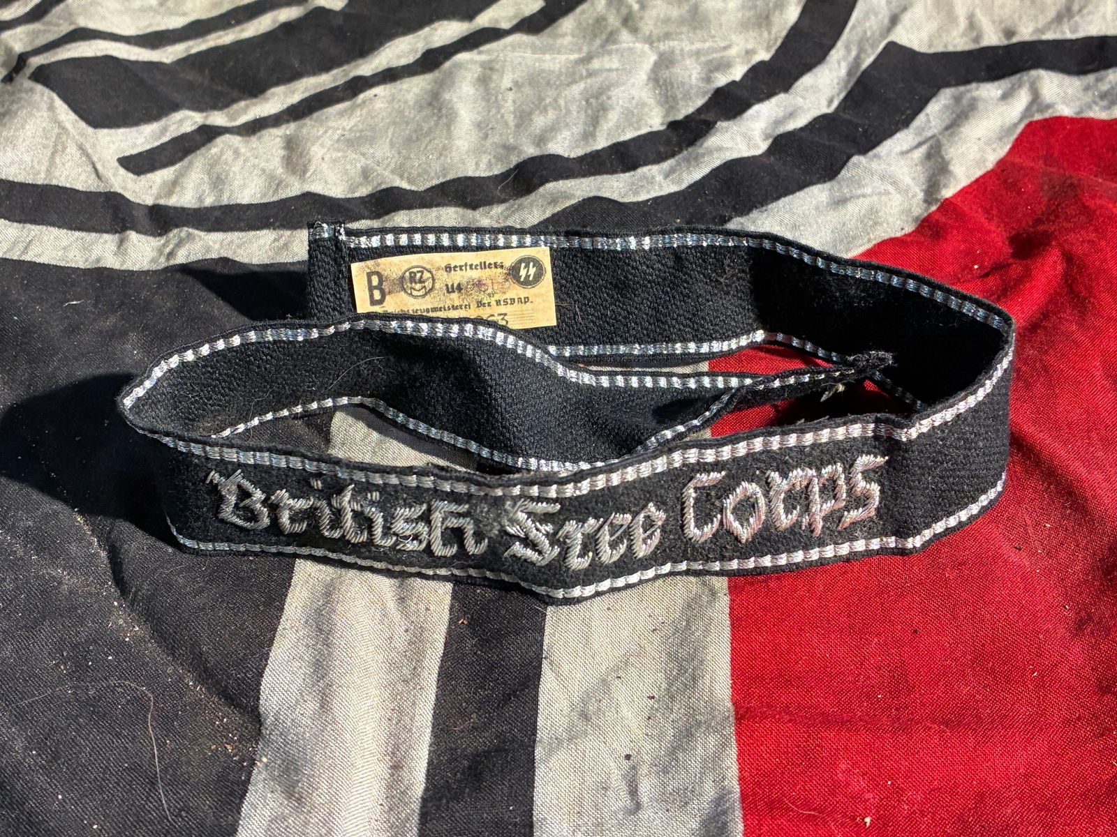 WW2 German Cuff Title of the British Free Corps (Alleged SS Volunteer Unit), with RZM/SS Paper Tag: This textile armband—embroidered “British Free Corps” in gothic script and bordered with silver-gray trim—represents an artifact associated with the little-known and short-lived British Fr