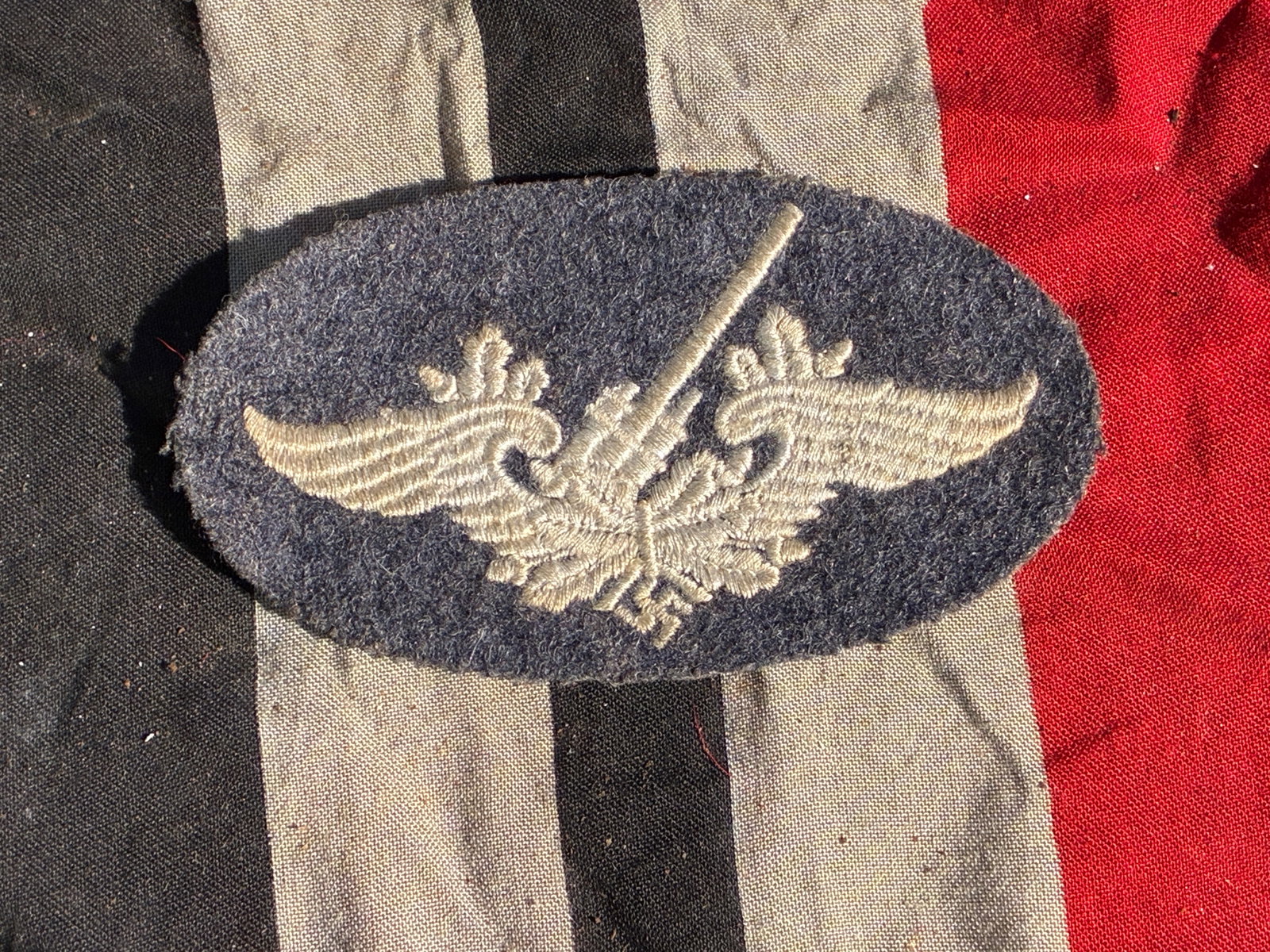 WW2 German Luftwaffe Flak Artillery Proficiency Badge (Cloth Version), Germany, 1939–1945: This oval cloth badge features an embroidered anti-aircraft cannon flanked by stylized wings, representing the Luftwaffe’s ground-based anti-aircraft units during the Second World War. Such cloth in