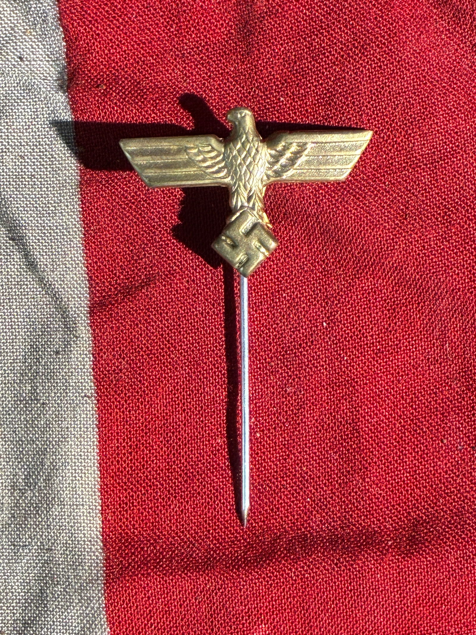 WW2 German National Eagle Stickpin (Third Reich Era), ca. 1933–1945: This small brass stickpin features the German national eagle emblem used by the Third Reich, depicted with outstretched wings perched atop a swastika within a wreath. Such miniature insignia were comm