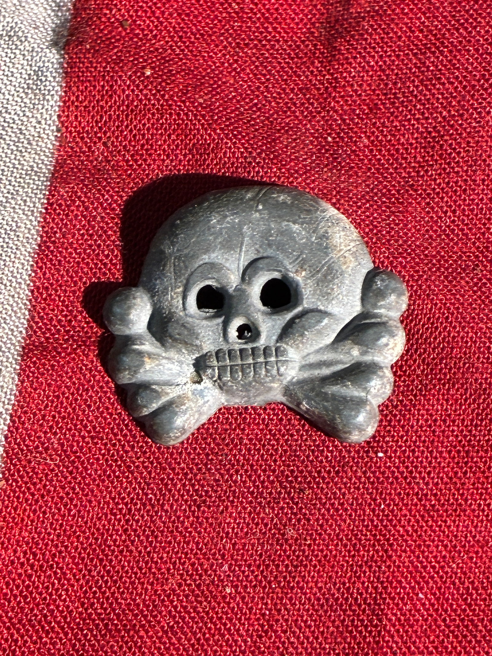 WW2 German Totenkopf SS Skull Cap Badge: This small metal badge features the traditional Totenkopf (skull and crossbones) design historically used by certain German military units. The emblem shows a rounded skull with hollow eyes positioned