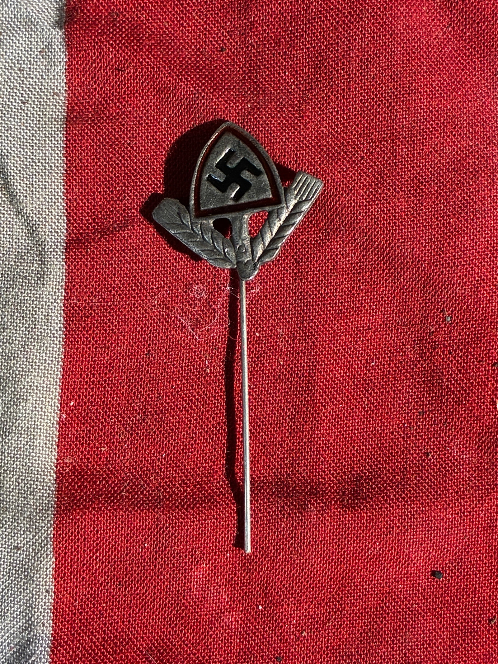 WW2 German National Socialist Agriculture Organization Stickpin (c. 1930s): This small stickpin features an agricultural motif combined with the insignia of the National Socialist regime in Germany during the 1930s. The design includes a triangular shield displaying the party