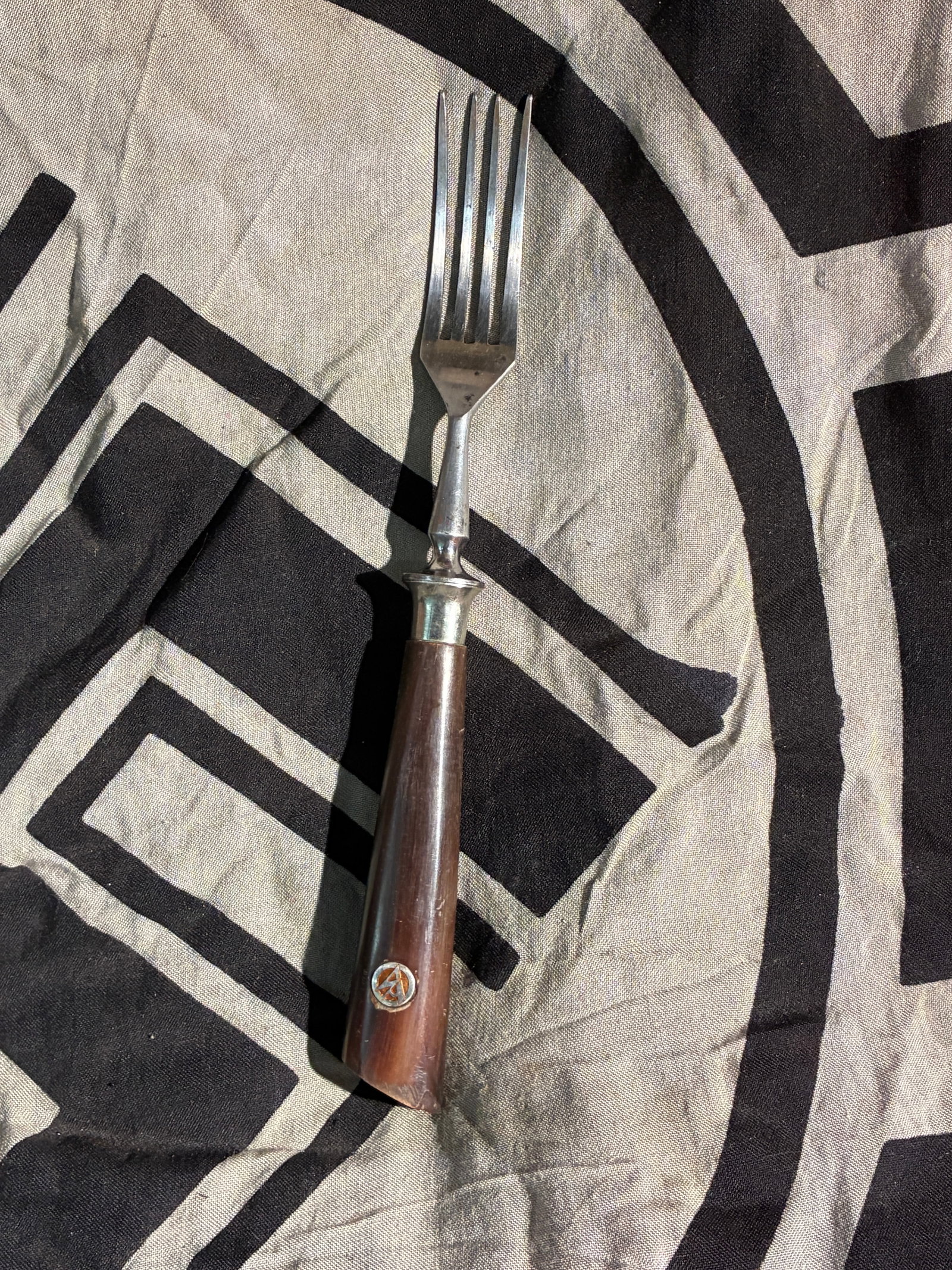 Dining Fork with Insignia Attributed to the National Socialist German Workers’ Party (NSDAP), c.: This eating utensil features a wooden handle inset with a small circular emblem resembling the insignia historically associated with the Sturmabteilung (SA), the paramilitary wing of the National Soci