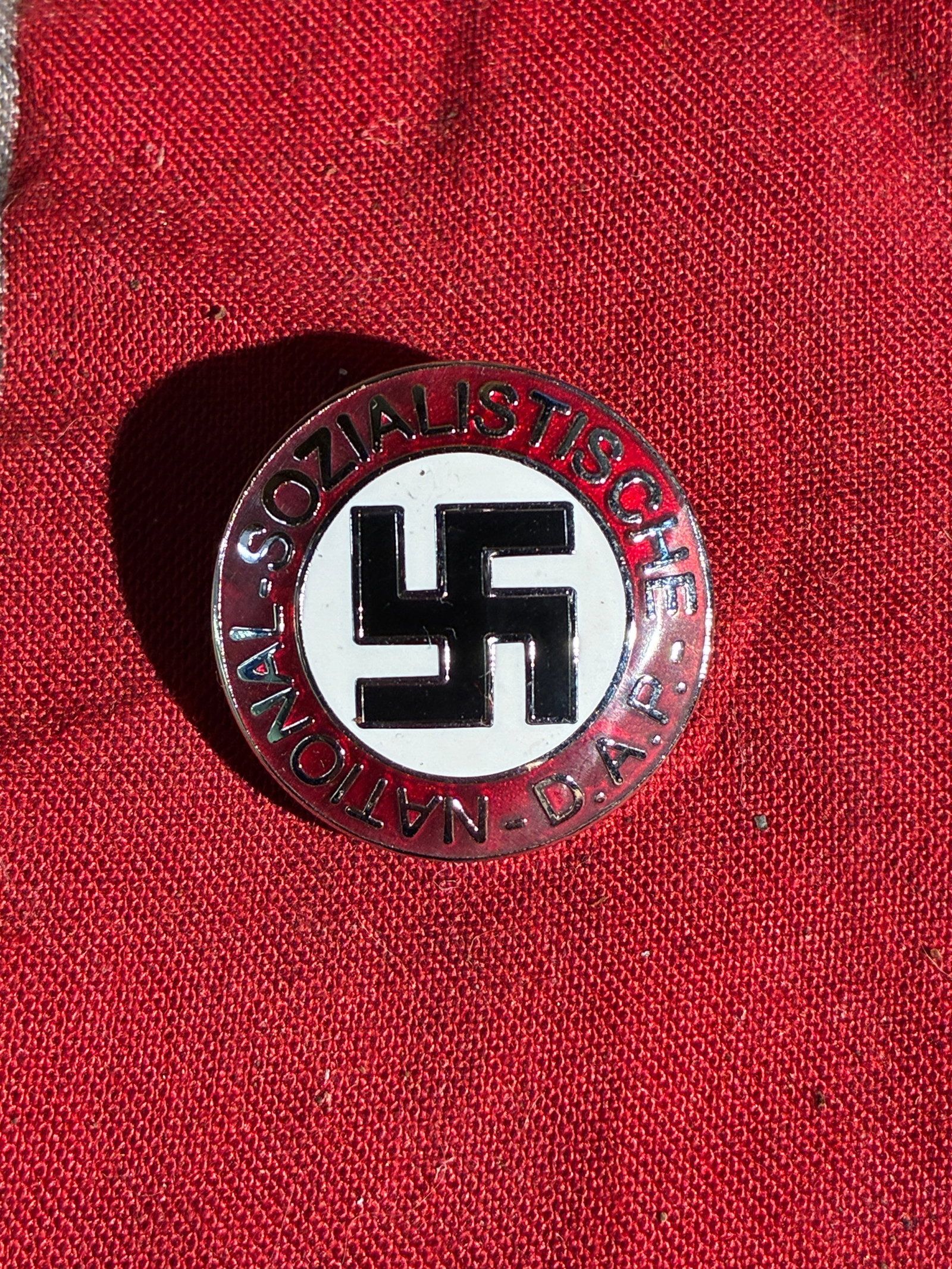 WW2 German NSDAP Party Membership Badge (1930s–1940s): This circular enameled badge features the swastika emblem at the center, surrounded by a red outer ring inscribed “National-Sozialistische D.A.P.” The design identified membership in the Natio