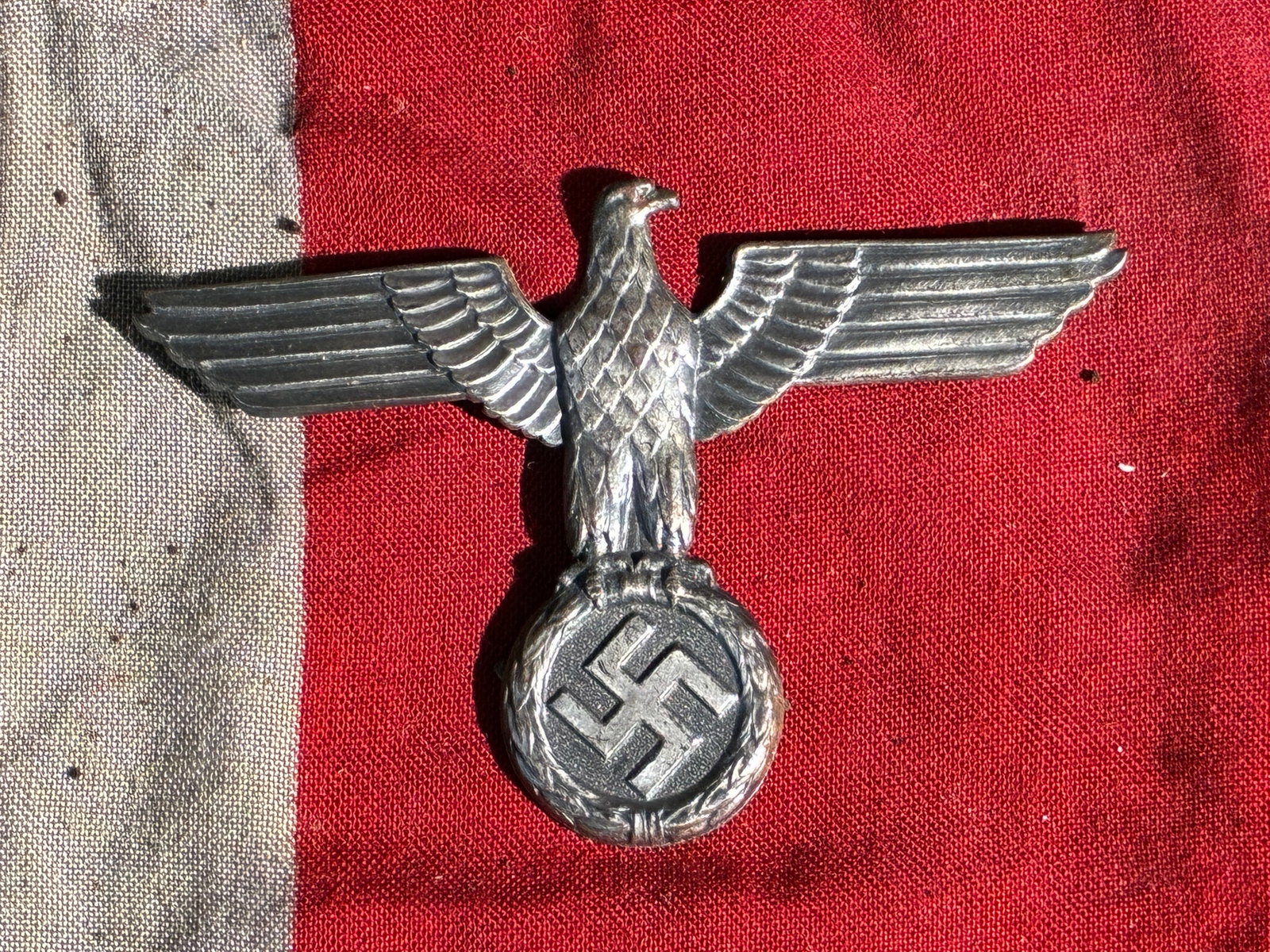 WW2 German National Emblem (Hoheitszeichen) — Cap Insignia, c. 1930s–1940s: This metal cap insignia features the German national eagle perched atop a wreath surrounding a swastika, a symbol appropriated and used by the National Socialist regime. Such emblems were worn on mili