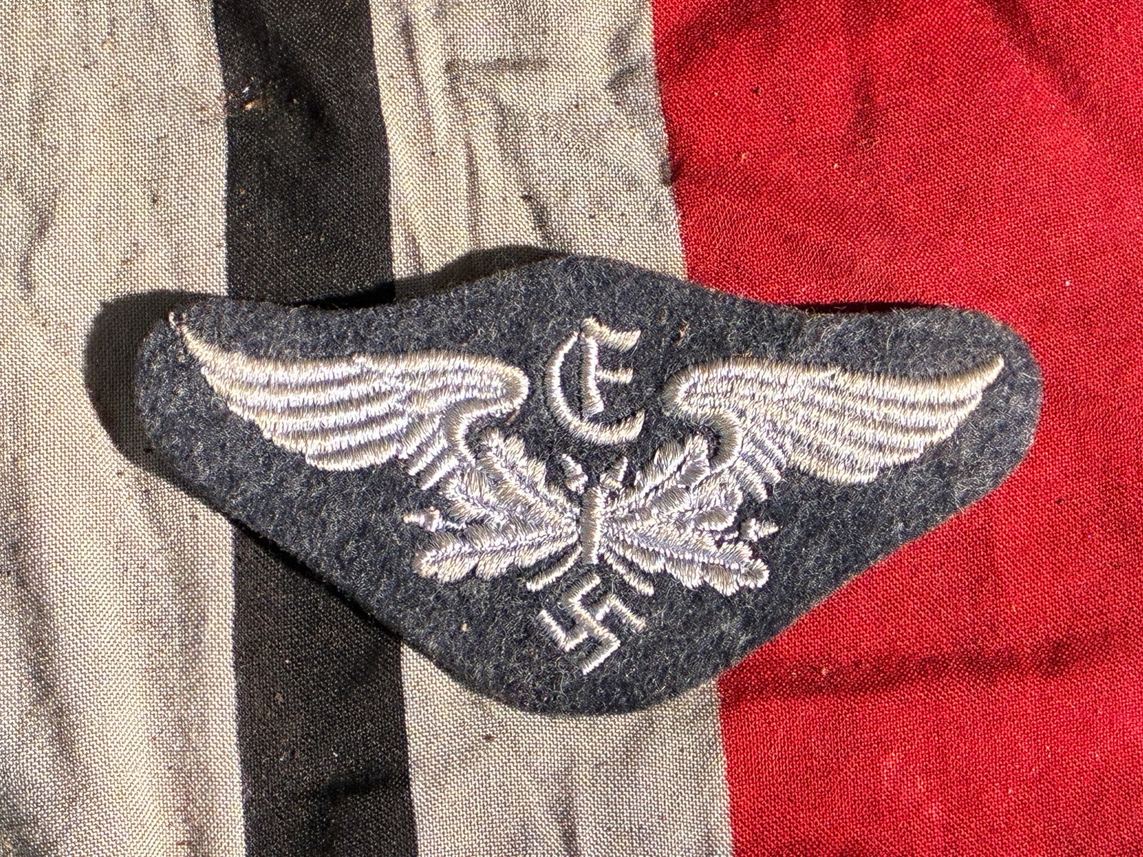 WW2 German Luftwaffe Medical Service Sleeve Insignia (c. 1939–1945): This cloth sleeve insignia belonged to the medical branch of the German Luftwaffe during the Second World War. Embroidered in silver-grey thread on dark blue wool, the emblem features outstretched win