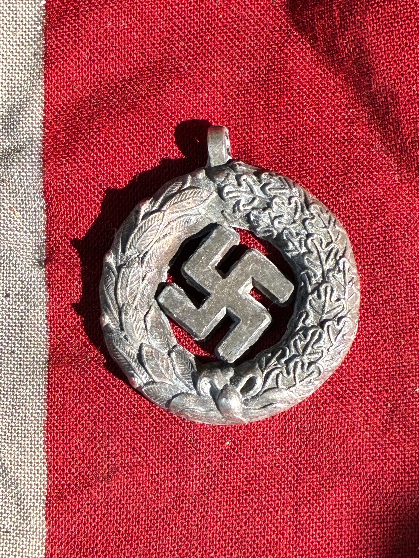 WW2 German Nazi Party Decorative Wreath Pendant with Swastika Motif (c. 1930s–1940s): This circular metal pendant features a cutout swastika surrounded by a detailed wreath combining oak leaves and laurel elements—symbolism commonly employed by the Nazi regime to represent militarism