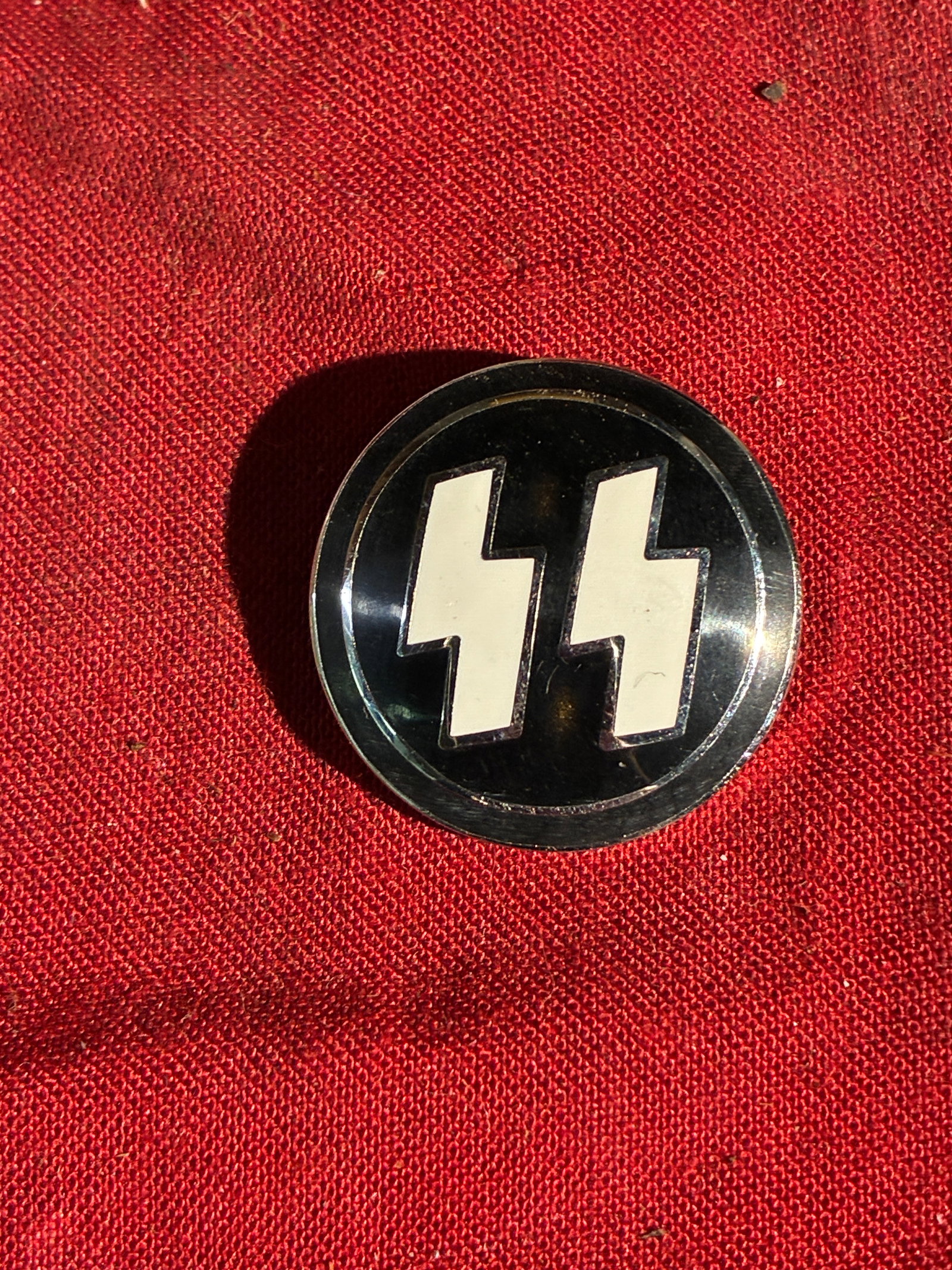 WW2 German Schutzstaffel (SS) Membership Badge – Late Pattern By RZM M1/4 Ges. Gesch.: This circular enameled badge represents a late-pattern insignia associated with the Schutzstaffel (SS), the paramilitary organization of the Nazi regime. Displaying the stylized SS “Sig” runes