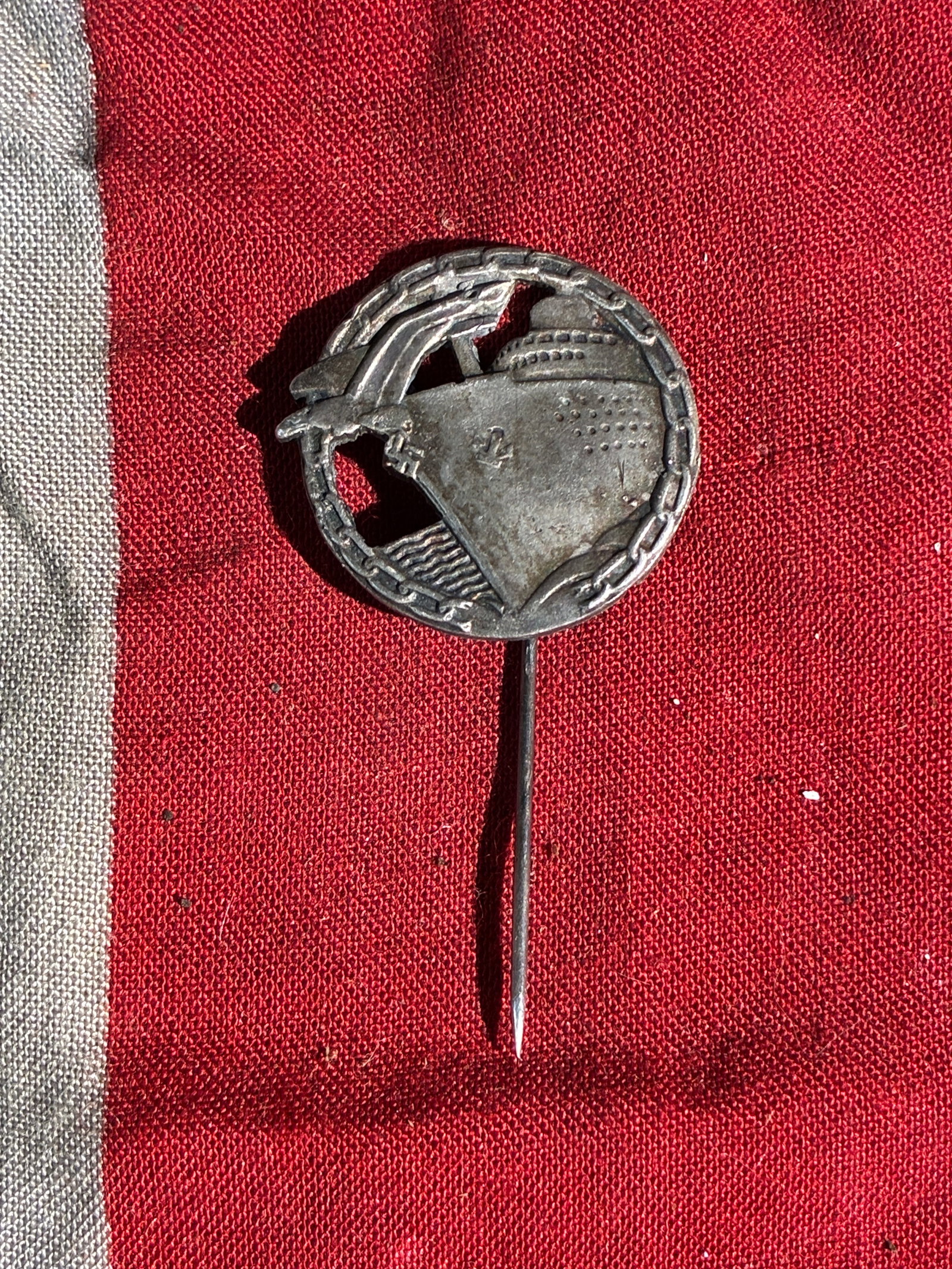 WW2 German Kriegsmarine Commemorative Stickpin (c. 1930s–1940s): This small metal stickpin depicts a stylized German naval warship framed by a chain-link oval border, a motif commonly associated with commemorative or patriotic naval badges produced during the era o