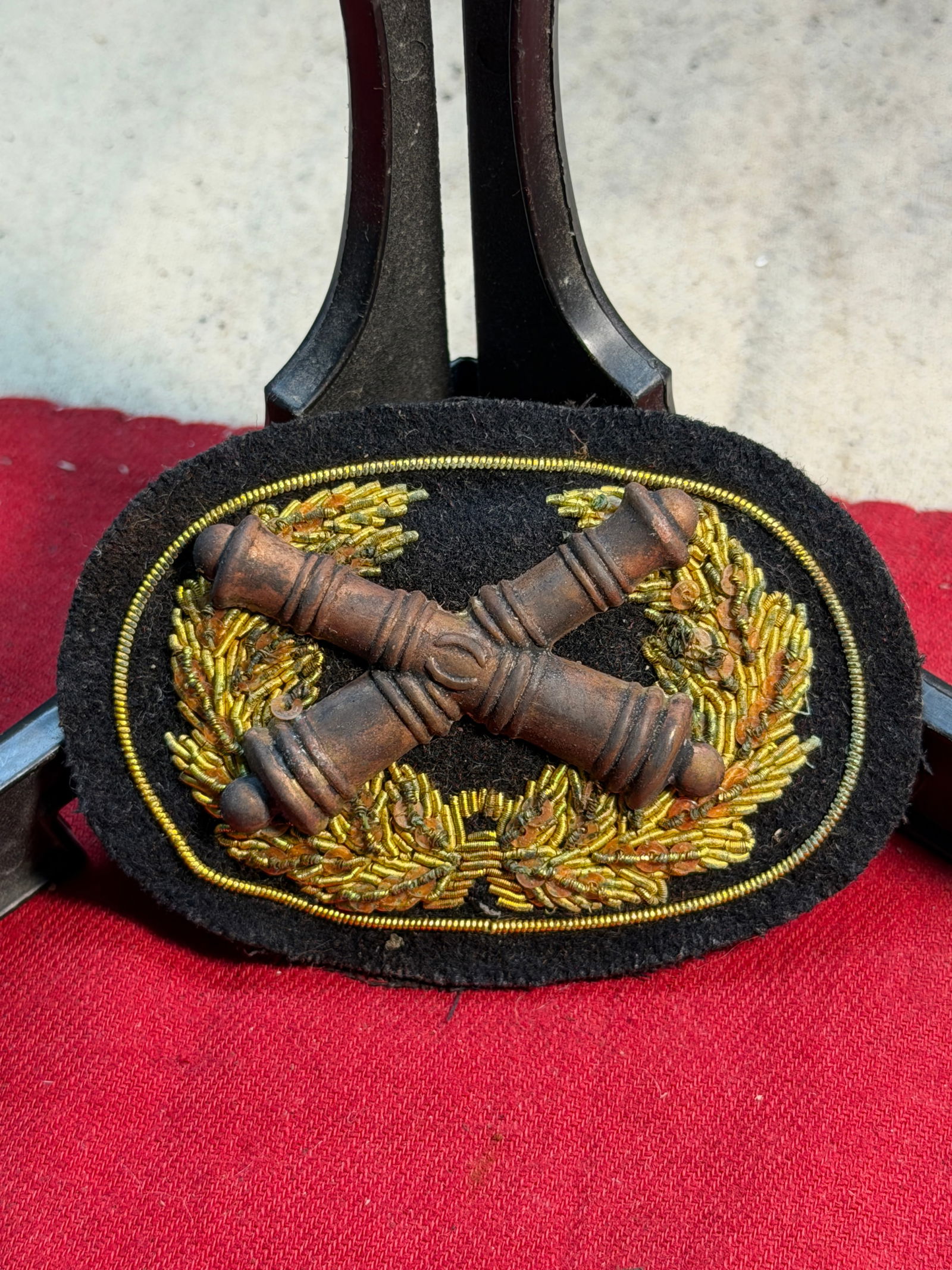 Civil War U.S. Artillery Officer’s Hand-Embroidered Crossed-Cannons Hat Insignia: This finely crafted Civil War–era U.S. Artillery officer’s hat insignia features a pair of cast crossed cannons mounted on a black wool backing, encircled by an intricate hand-embroidered wreath o
