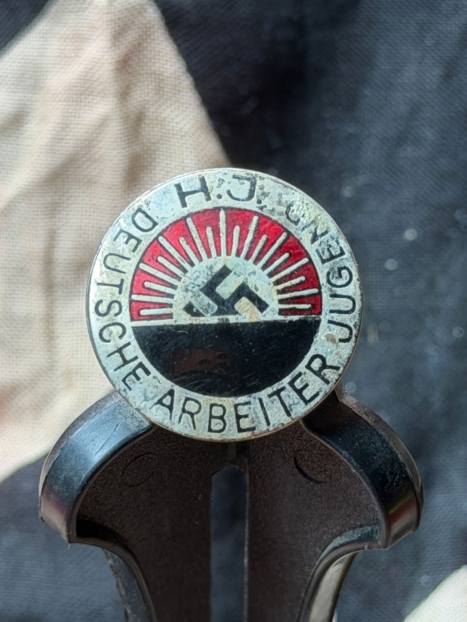 WW2 German Hitler Youth Lapel Badge (“Blut und Boden / Deutsche Arbeit??), Nazi: This enamel lapel badge is associated with the Hitler Youth (Hitlerjugend, HJ), the official youth organization of Nazi Germany. The circular design features a rising sun motif over a plow and field,