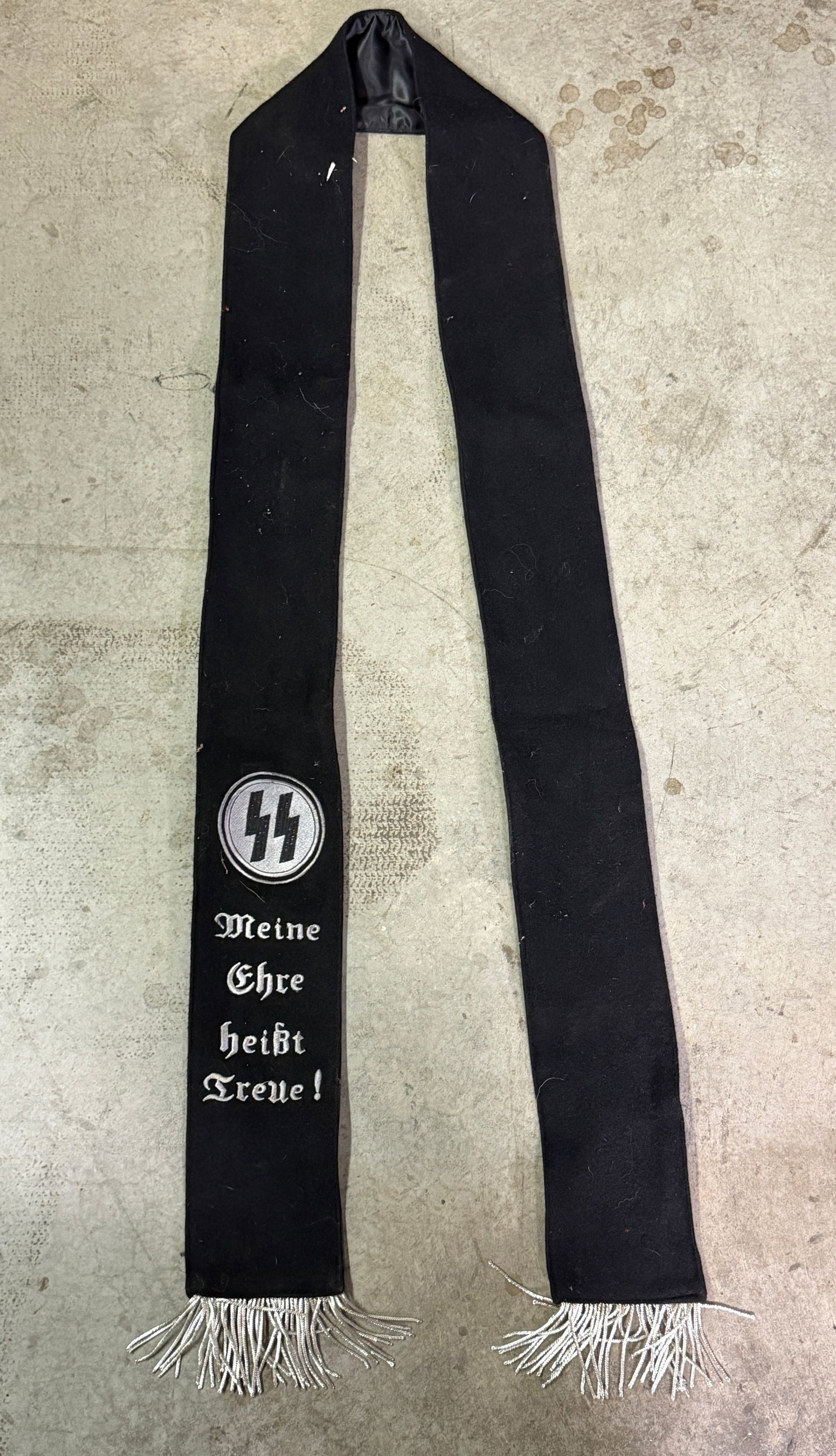 WW2 German SS Funeral and Mourning Sash (Trauerschärpe der SS): SS funeral and mourning sash used during the period of Nazi Germany. Constructed of black wool or felt with a satin-lined reverse and silver metallic fringe, the sash bears the embroidered SS runic em