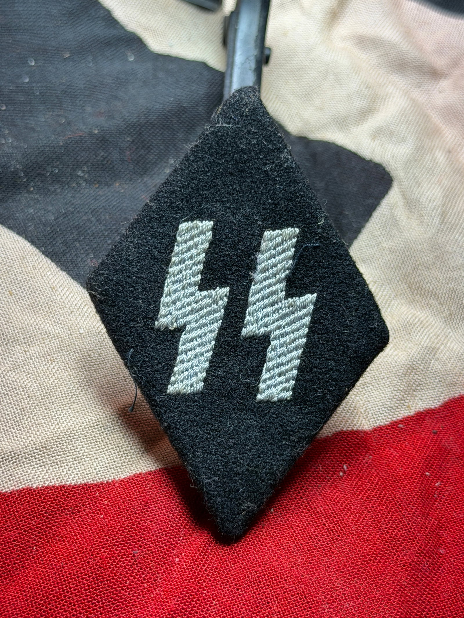 WW2 German SS Enlisted Rank Collar Tab (Double Sig Rune): Collar tab bears the distinctive Sig runes associated with the Schutzstaffel (SS), a paramilitary organization of Nazi Germany. The paired runic symbols, rendered in silver-gray thread on a black fiel