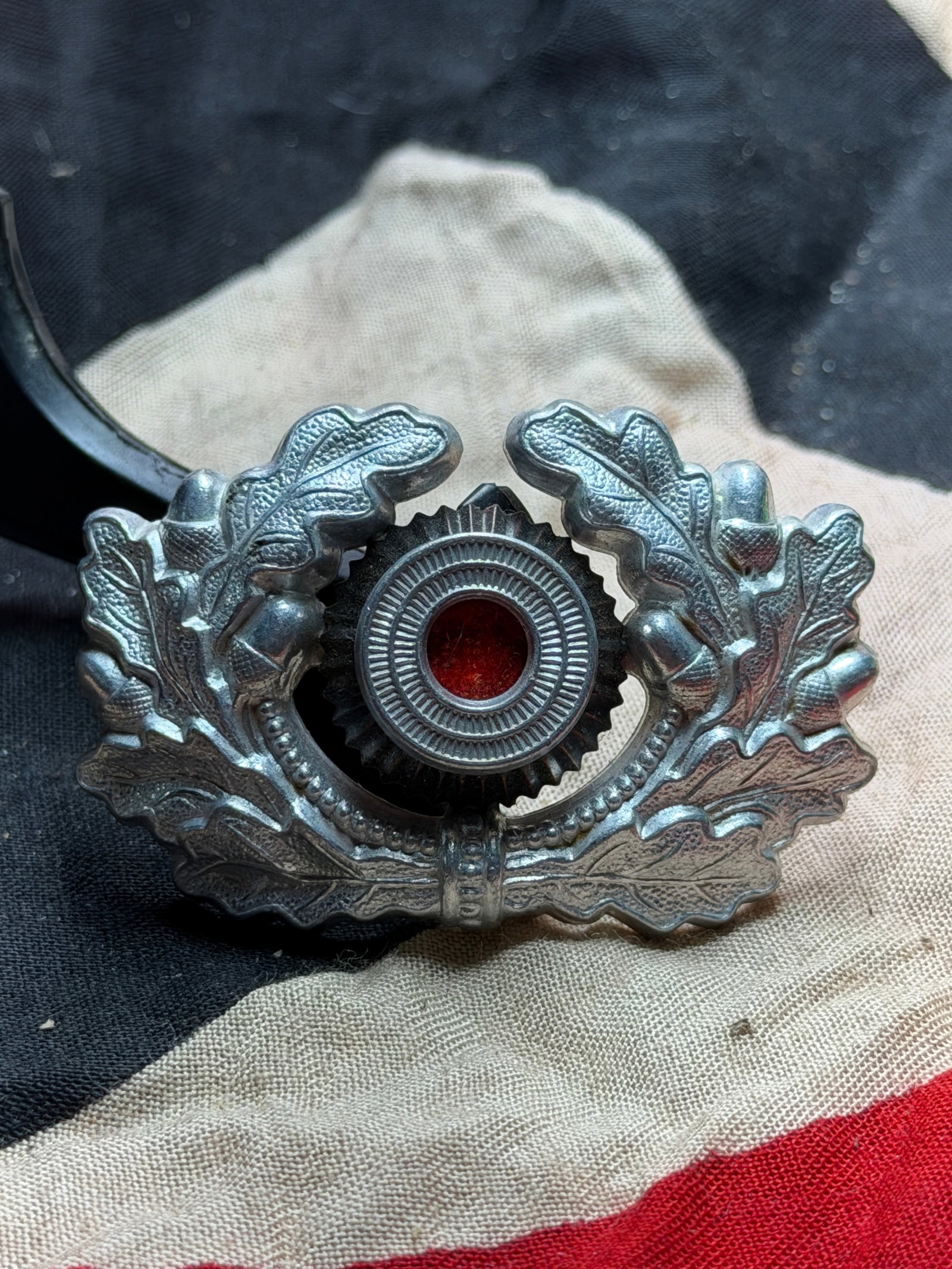 WW2 German Third Reich–Era Award Badge with Oakleaf Wreath: This metal award badge dates to the period of National Socialist Germany and features a symmetrical oakleaf wreath encircling a central roundel with red enamel. The oakleaf motif—long associated wit
