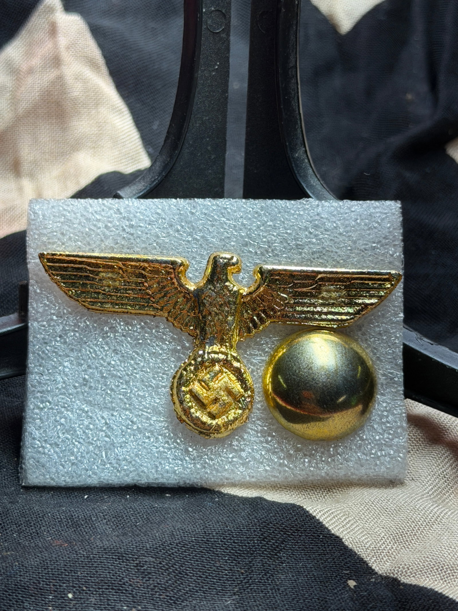 WW2 German National Eagle Cap Insignia with Retaining Button: This gilt-finished metal insignia depicts the German national eagle grasping a wreath enclosing a swastika, a standardized emblem used by the German state and its military and paramilitary organizatio
