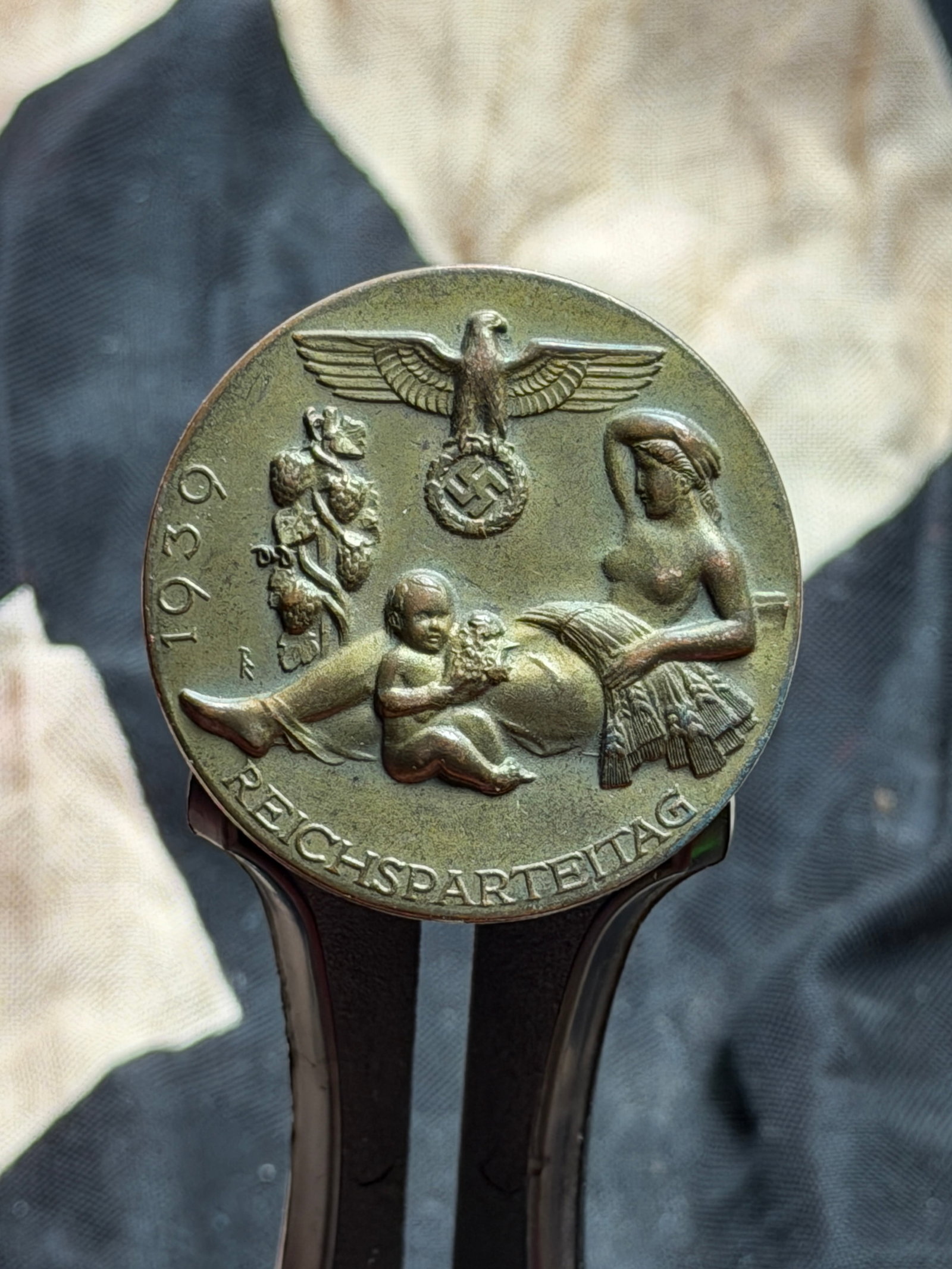 WW2 German Reichsparteitag 1939 Commemorative Badge (Reich Party Rally Tinnie): This metal commemorative badge, commonly known as a Reichsparteitag tinnie, was issued for the 1939 Nazi Party Rally (Reichsparteitag) held in Nuremberg. The obverse features allegorical imagery consi