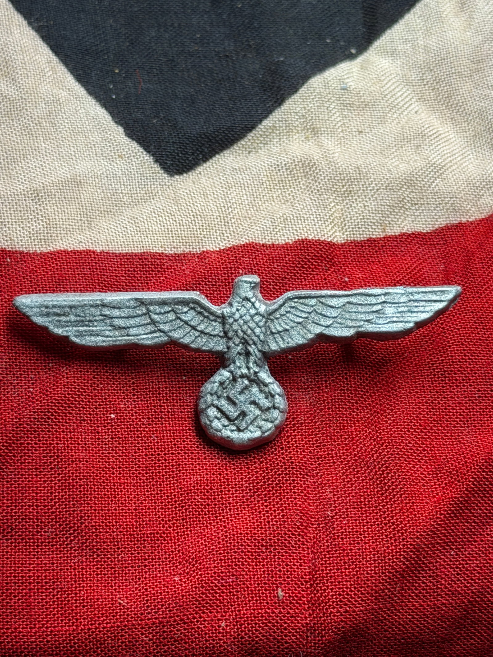 WW2 German Cap Eagle Insignia (Hoheitsabzeichen): This small cast-metal eagle insignia represents the Hoheitsabzeichen (“national emblem”) used on caps and uniforms in Nazi Germany between 1933 and 1945. The outstretched eagle clutching a wre