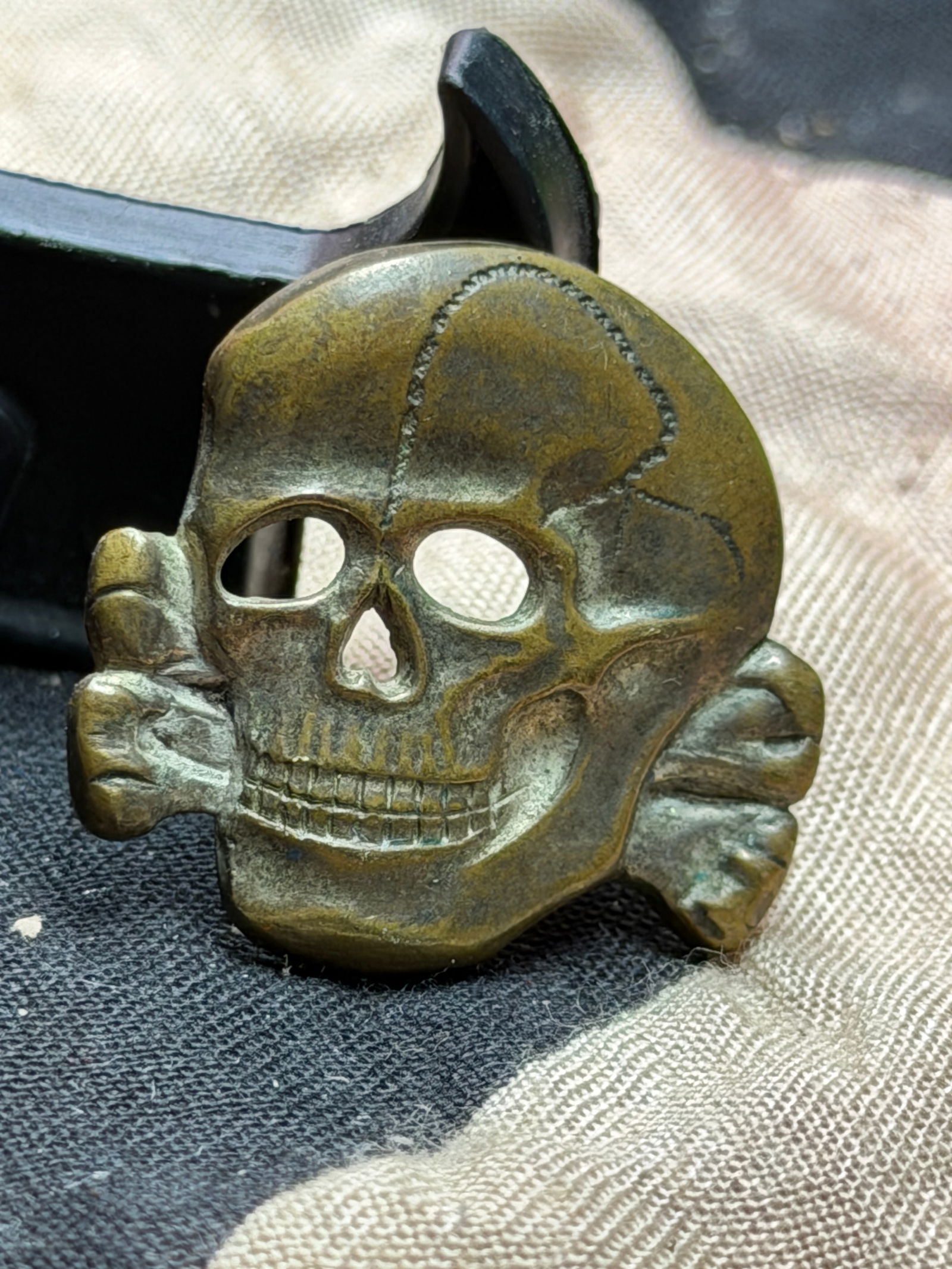 WW2 German SS Totenkopf Cap Insignia (Skull and Crossbones): This metal cap insignia depicts the Totenkopf (“death’s head”), a skull with crossed bones, an emblem historically associated with elite military units and later adopted by the Schutzstaffel
