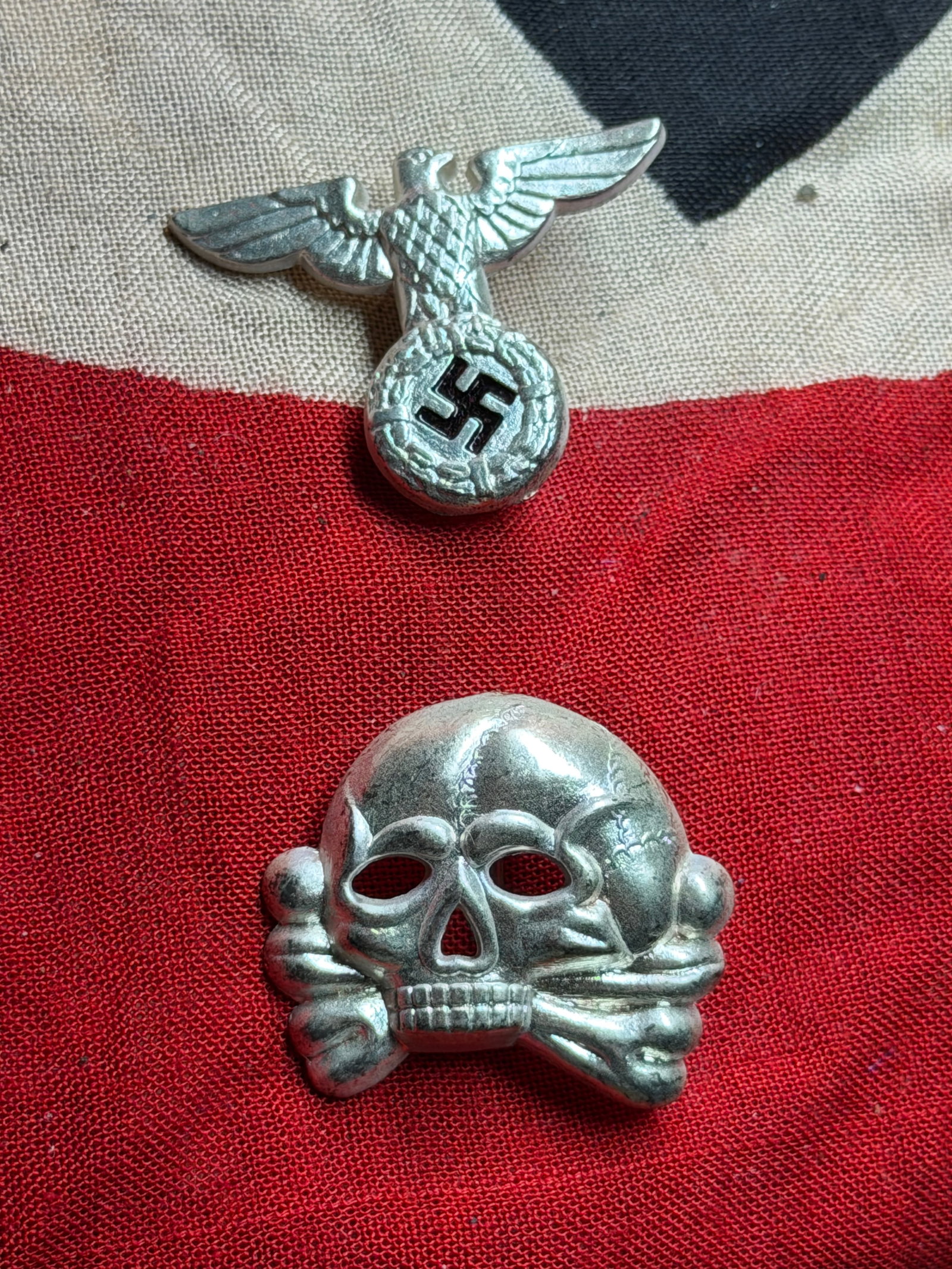 WW2 German Insignia of the Schutzstaffel (SS): Cap Eagle and Totenkopf Emblems: This display presents two emblematic components of the Schutzstaffel (SS), one of the principal organizations of the National Socialist regime in Germany between 1933 and 1945. Shown here are a silver
