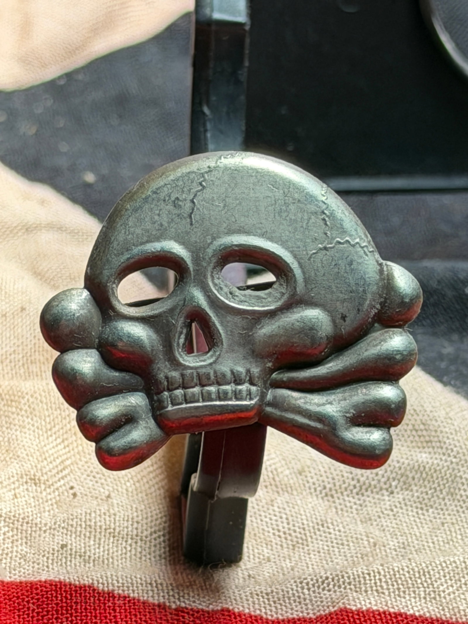 WW2 German Totenkopf (Death’s Head) Cap Insignia, Allgemeine SS: This metal Totenkopf (Death’s Head) cap badge is a Third Reich–era German insignia associated with the Allgemeine SS, produced in the 1930s–early 1940s. The stylized skull with crossed bones ben