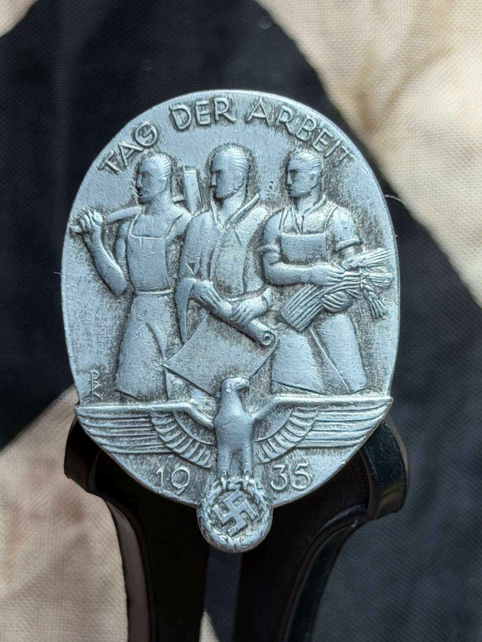 WW2 German “Tag der Arbeit?? (Day of Labor) Commemorative Badge, Germany, 1935: This badge was issued in 1935 to commemorate the “Tag der Arbeit” (Day of Labor), a state-sponsored celebration observed annually on 1 May in Nazi Germany. The obverse depicts three idealized 
