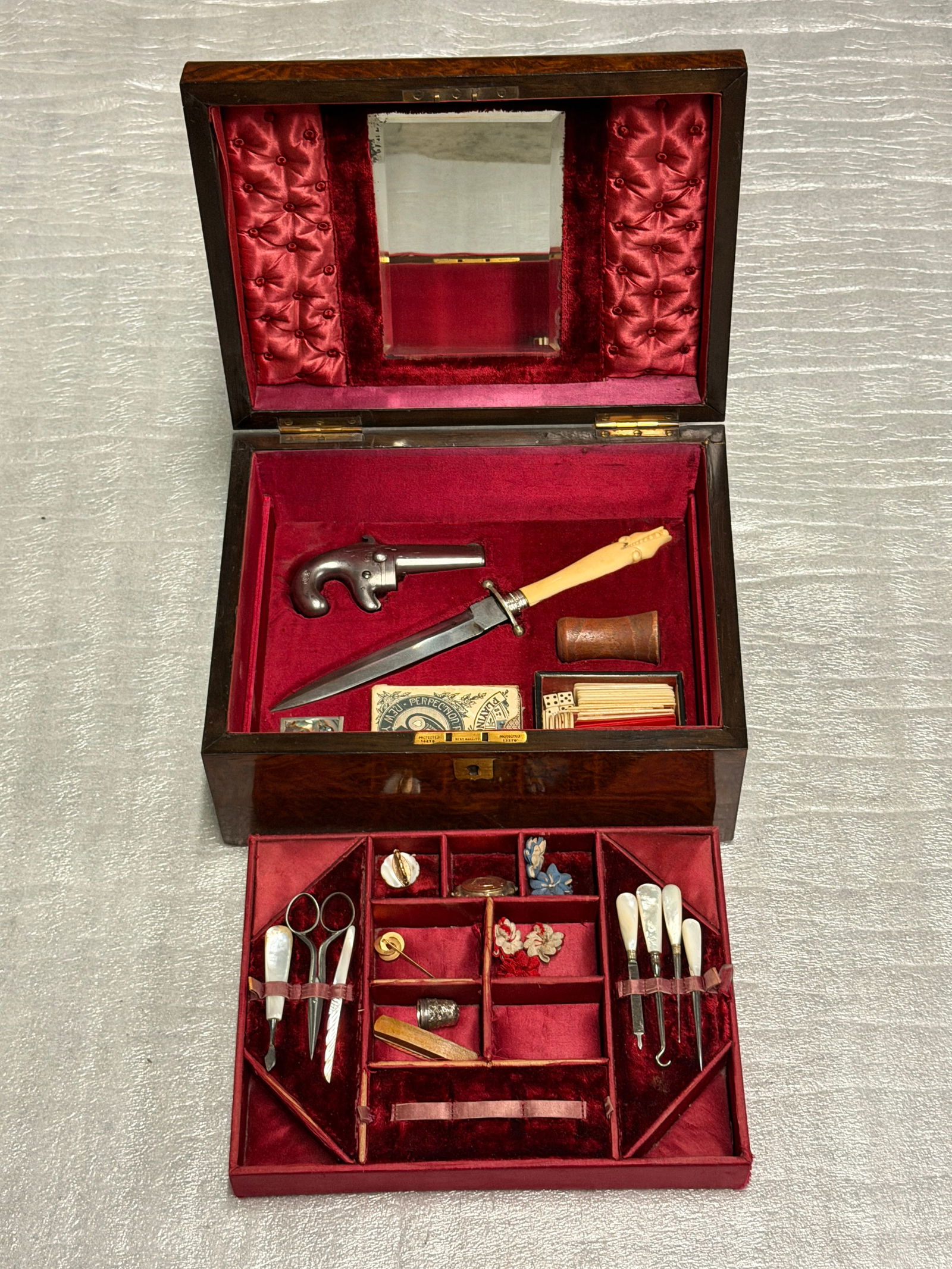 A Lady’s Traveling Necessaire with Arms: Presentation Casket to Miss Howard, c. 1840–1860: This richly appointed traveling casket represents a rare and revealing convergence of personal care, leisure, and self-defense in the mid-19th century. Veneered in finely figured wood and lined in dee