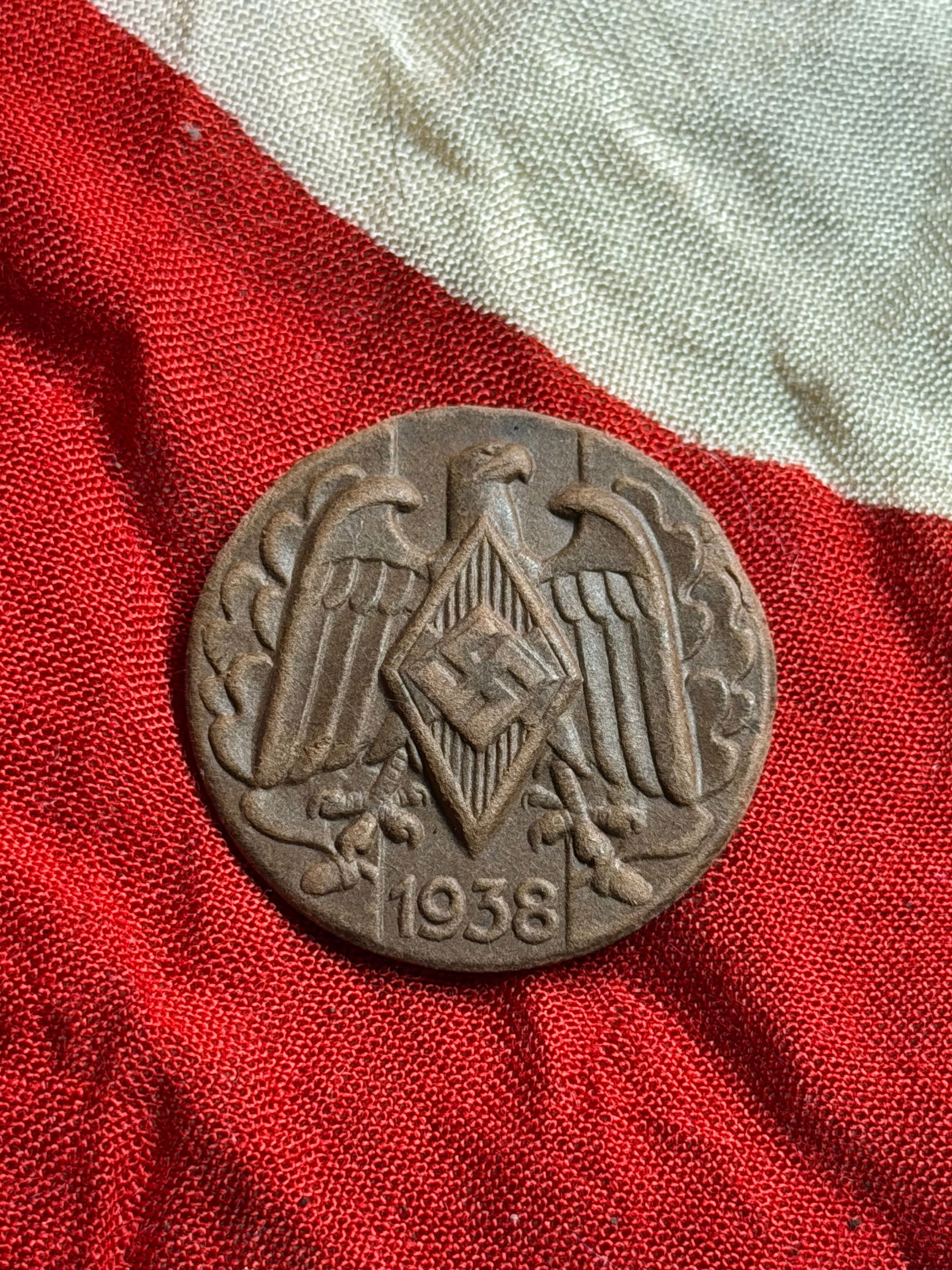 WW2 German Hitler Youth Membership Badge 1938: This round metal badge dates to 1938 and features a stylized German eagle grasping a diamond-shaped emblem bearing the insignia of the Hitler Youth (Hitlerjugend), the state-sponsored youth organizati