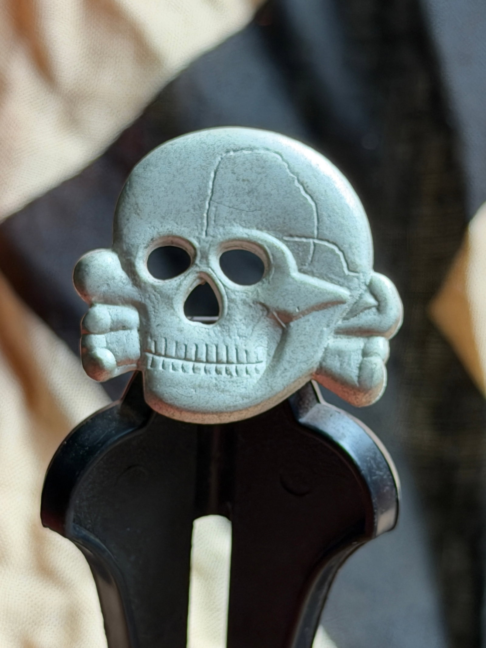 WW2 German Skull-and-Crossbones Badge (Totenkopf Motif): This small metal badge depicts a stylized human skull with crossed bones, a motif historically known as the Totenkopf (“death’s head”). Cast in a pale alloy and finished with a matte, light-