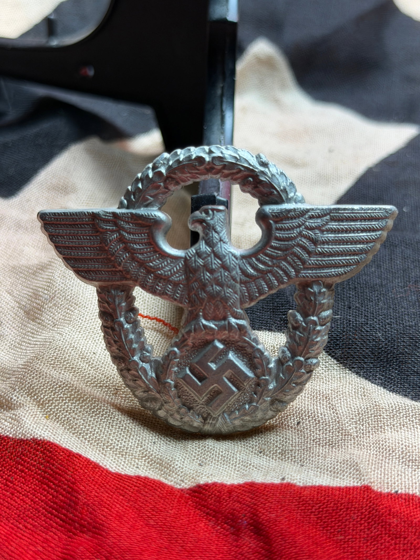 WW2 German Police Visor Cap Eagle Insignia (Schutzpolizei / Ordnungspolizei): This metal insignia is identified as a World War II German Police visor cap eagle, worn by members of the Ordnungspolizei (Order Police), including the Schutzpolizei (municipal police), during the per