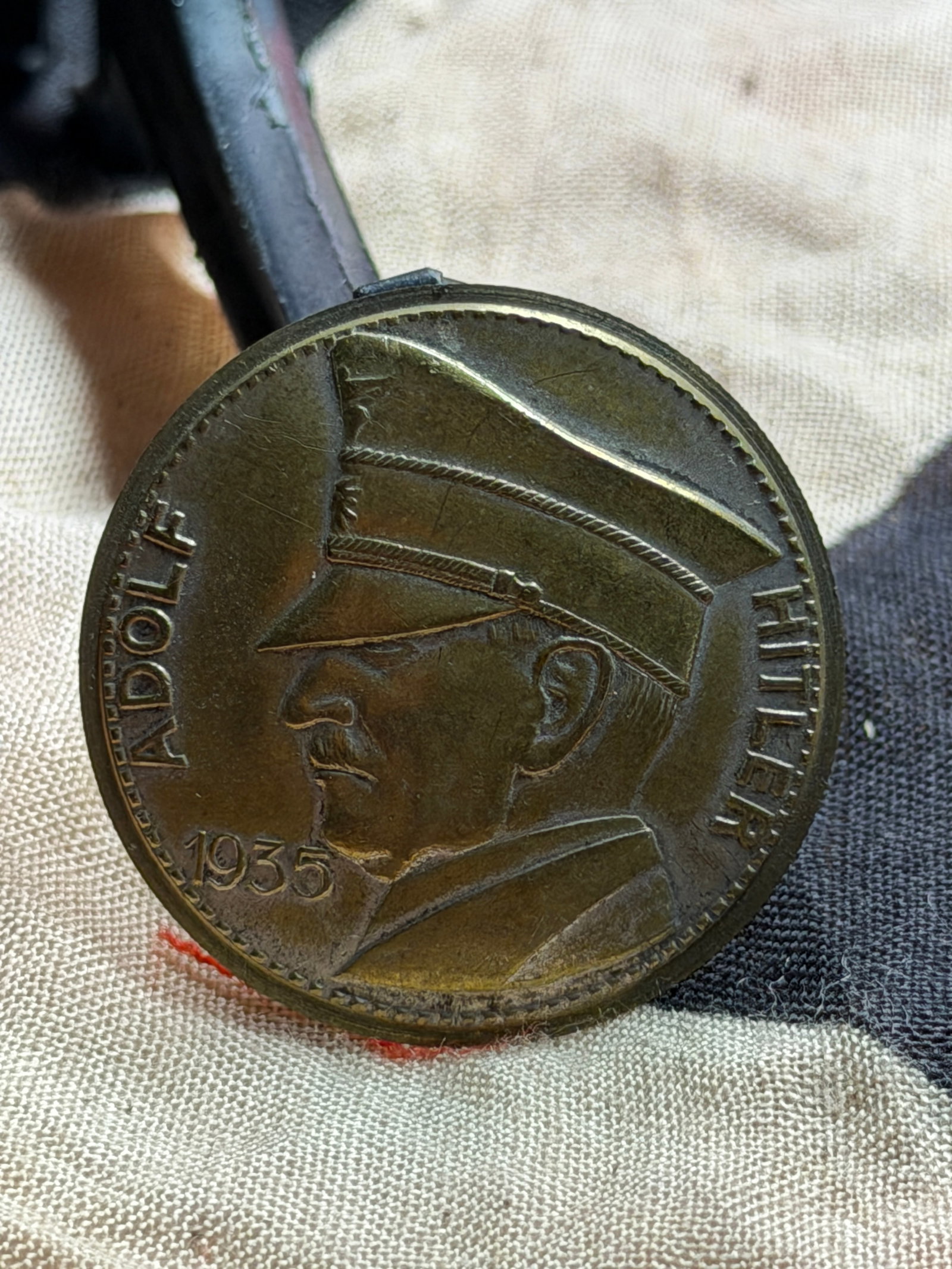WW2 Germany, Third Reich: Adolf Hitler Commemorative Coin (1935): This round metal coin bears a left-facing portrait of Adolf Hitler, surrounded by the inscription “ADOLF HITLER” and dated 1935. The obverse reflects the visual style commonly employed in Nati