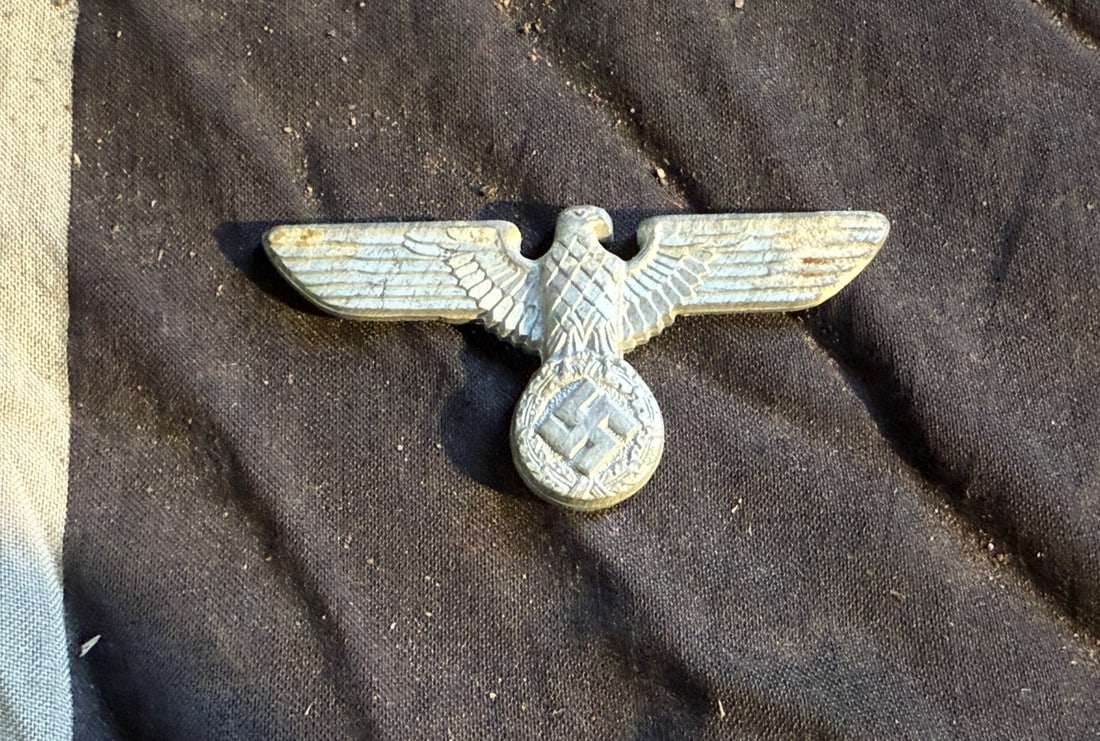 WW2 German National Socialist Eagle Insignia (Reichsadler): This metal insignia depicts the Reichsadler (Imperial Eagle) clutching a wreath enclosing a swastika, a standardized emblem used by National Socialist organizations in Germany between 1933 and 1945. C