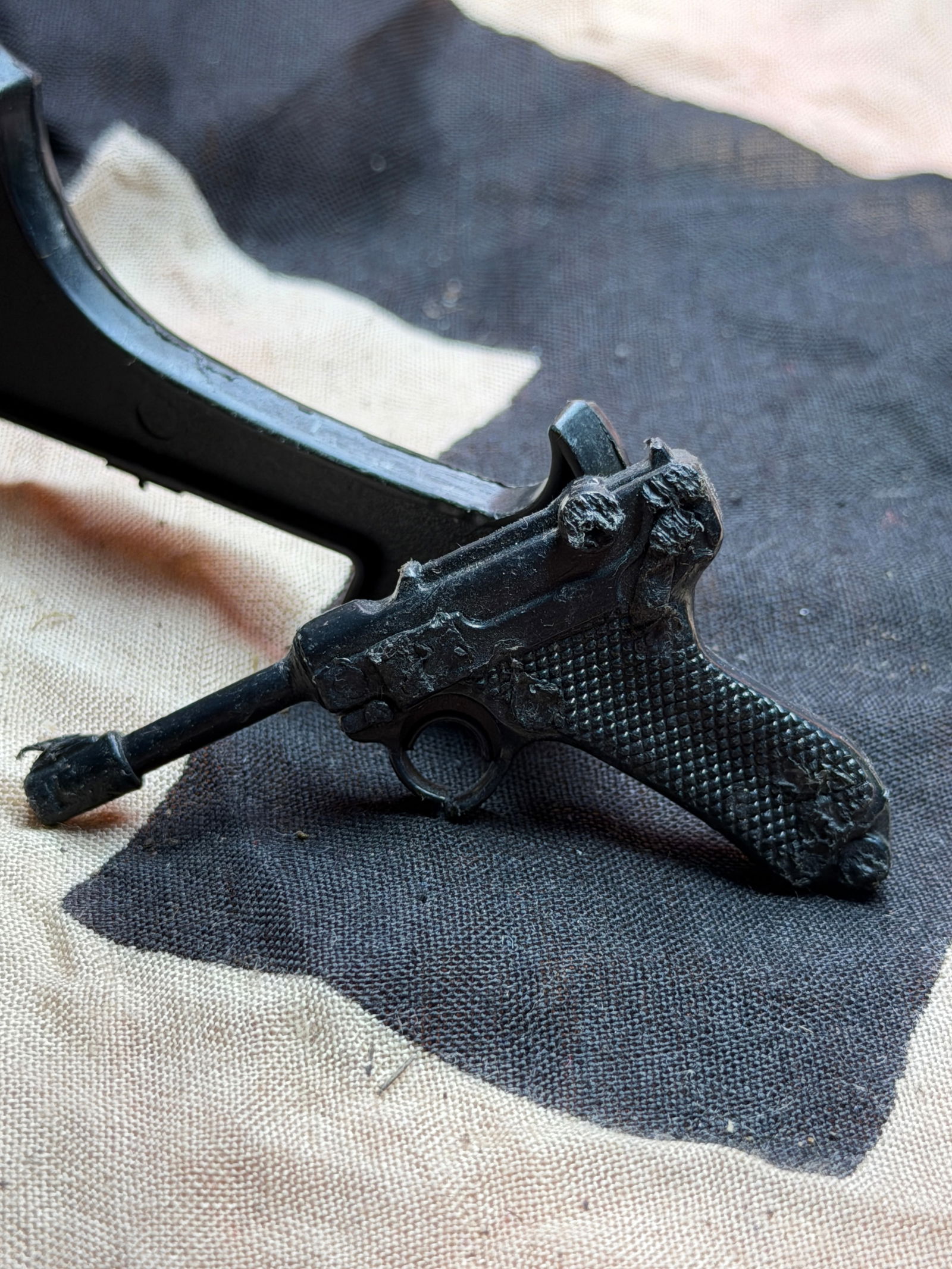 WW2 German Miniature Pistol Charm in the Form of a Luger P08: This small cast-metal charm depicts a stylized miniature of the German Luger P08 pistol, one of the most recognizable handgun designs of the early 20th century. Rendered with simplified mechanical det