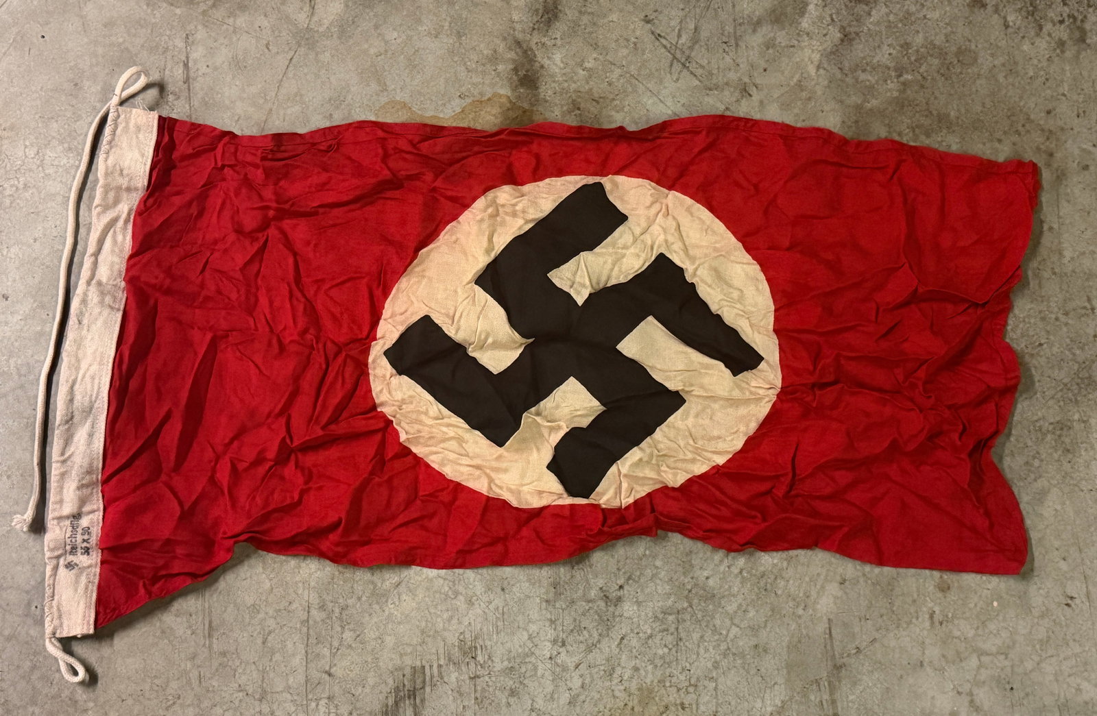 WWII-Era German National Flag (Third Reich), Red Field with Black Emblem in White Circle: German national flag from the World War II era, identifiable by its red field with a central white circle containing a black emblem. The flag is constructed of lightweight woven fabric and features a