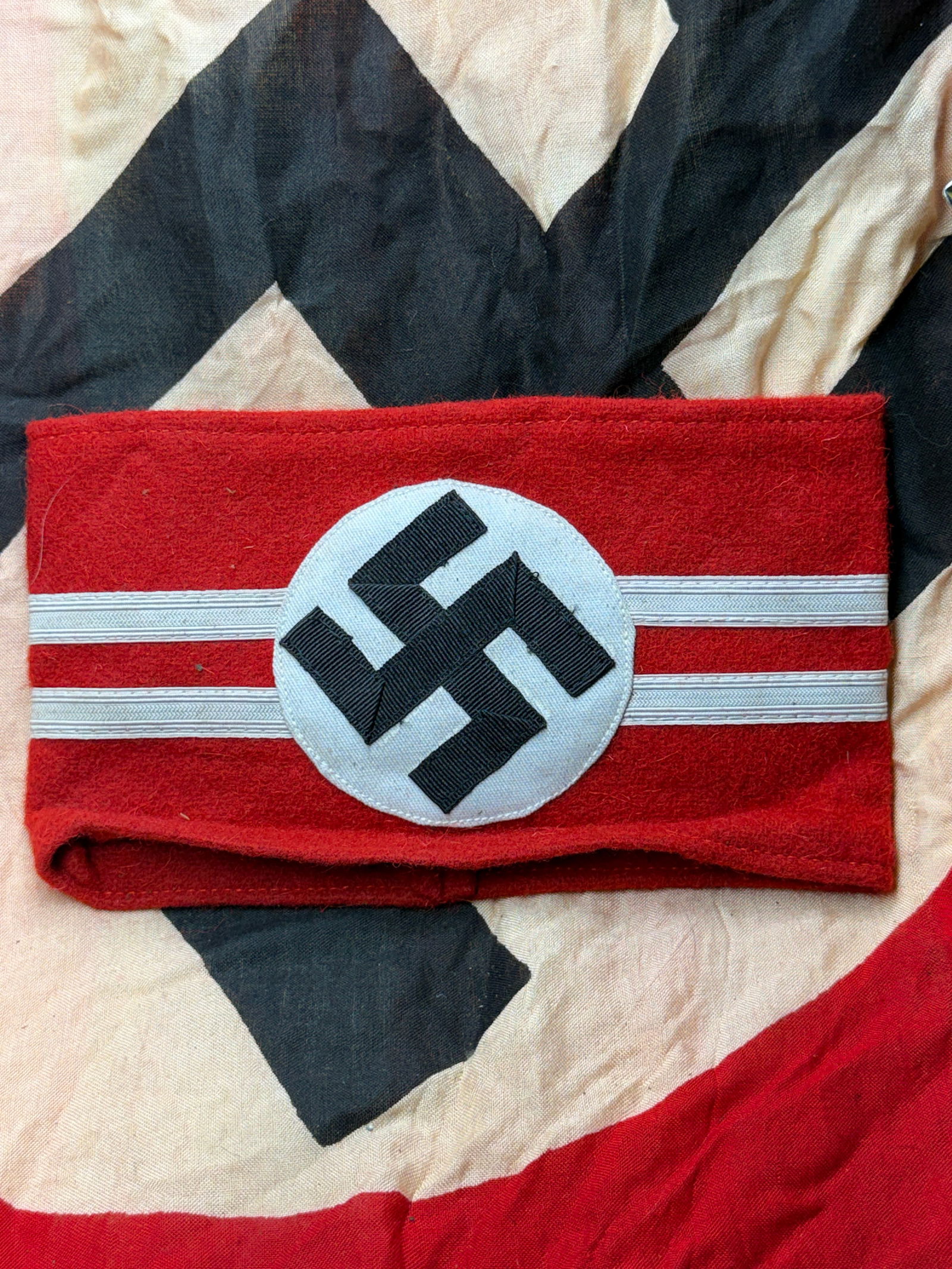 WW2 German National Socialist Armband (Reichsleitung Pattern with RZM Tag): WW2 German National Socialist Armband (Reichsleitung Pattern with RZM Tag). Constructed from red wool felt, it features a white roundel bearing a black swastika, flanked by two horizontal silver-gray