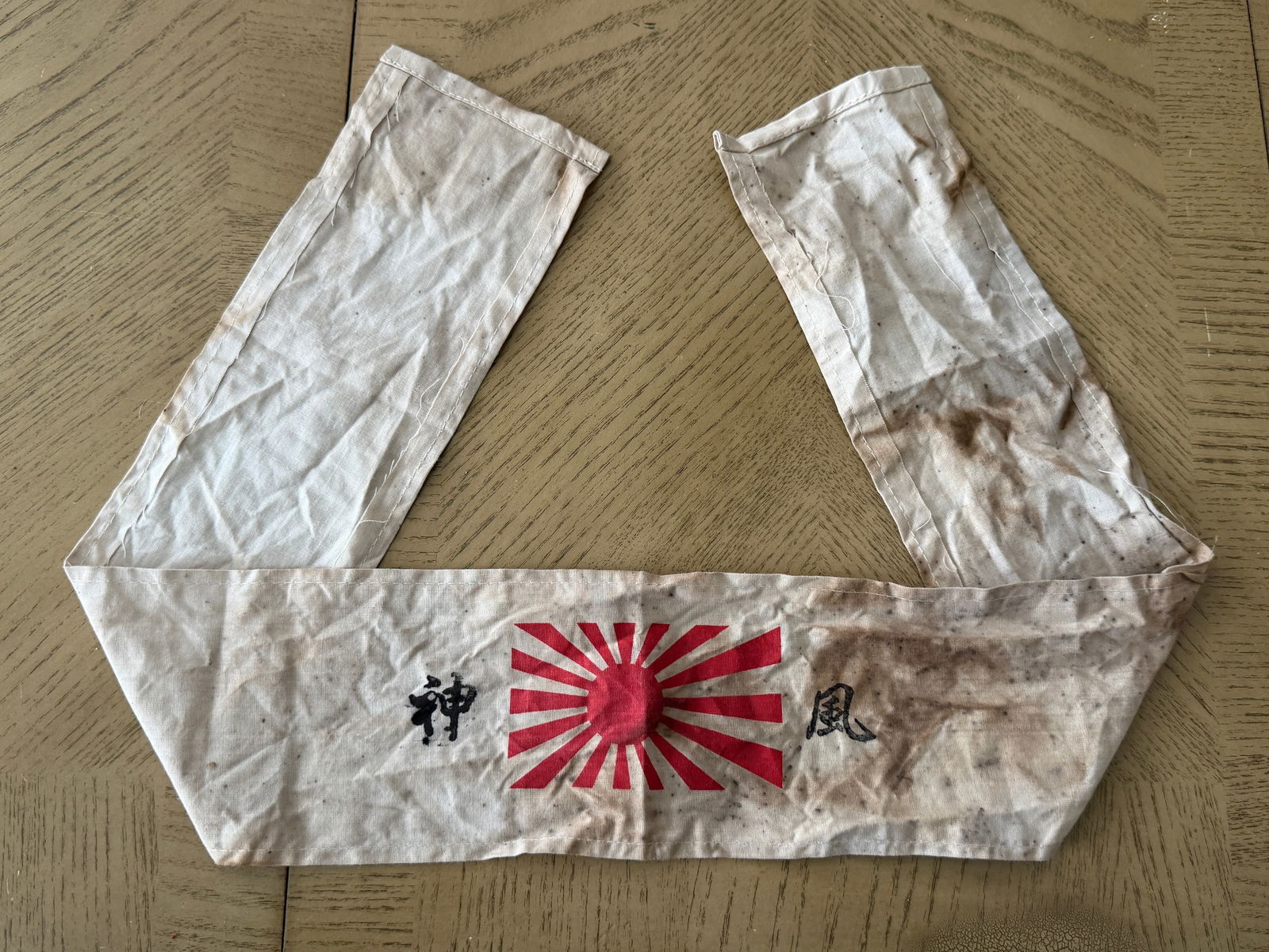 WWII Imperial Japanese Rising Sun Hachimaki Headband – Field-Used Cotton: World War II–era Imperial Japanese Army hachimaki (headband), featuring the iconic red Rising Sun emblem flanked by black hand-applied Japanese characters. Constructed from lightweight cotton, this