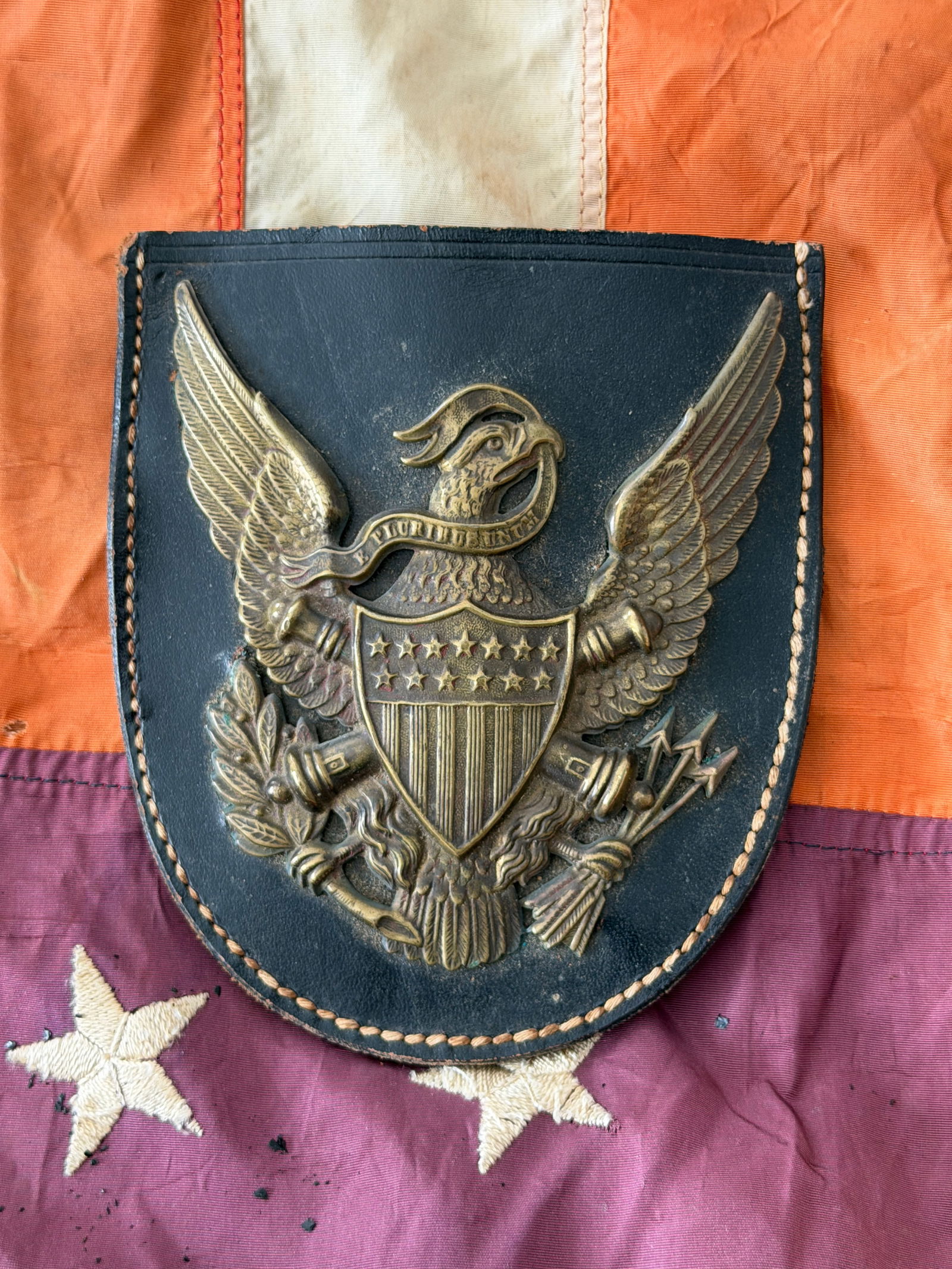 U.S. Army Cartridge Box Flap with Federal Eagle Breastplate, Indian Wars Era, c. 1866–1890: This leather cartridge box flap dates to the post–Civil War Indian Wars era and features a prominently mounted brass Federal eagle breastplate. The eagle bears a shield of stars and stripes and gras